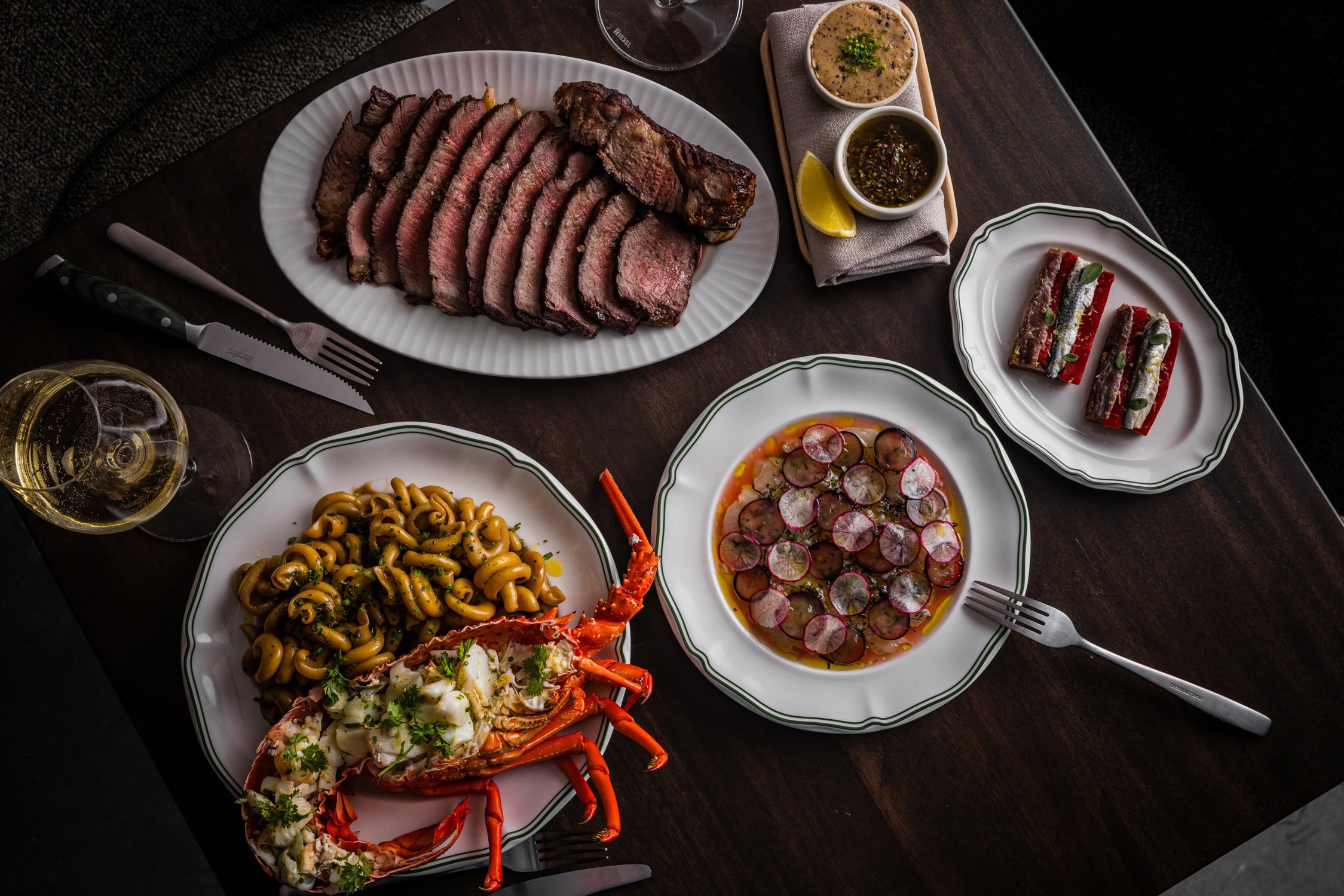 Overhead spread of dry-aged steak lobster pasta radish salad and sardines with white wine at The Hideaway Bondi Junction Sydney