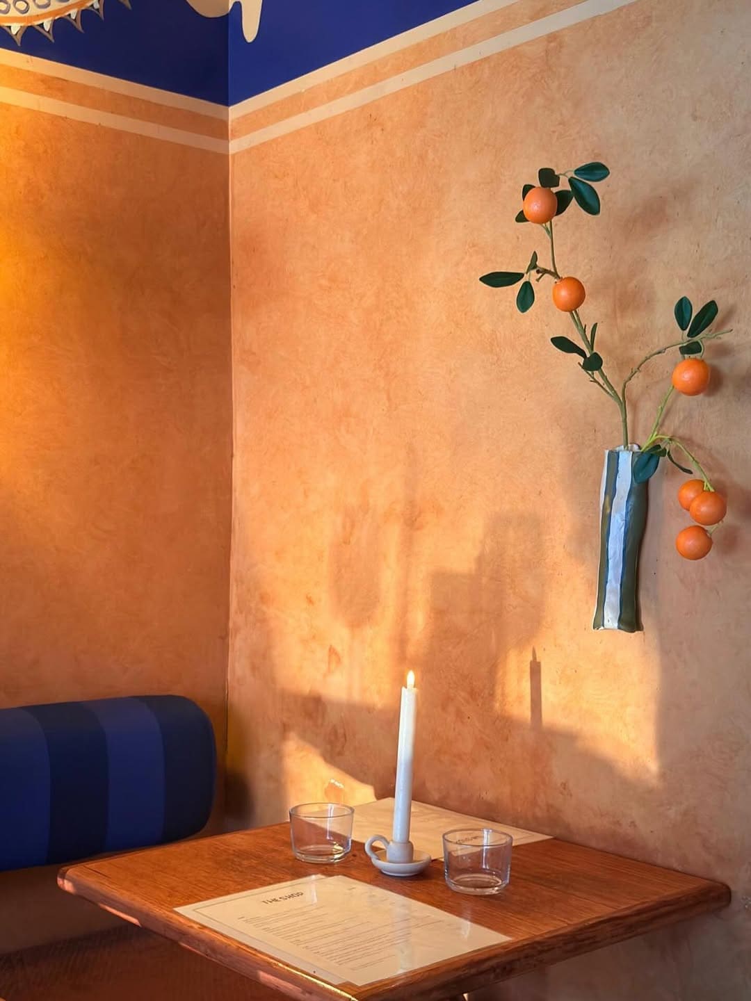 Warm terracotta plastered wall with cobalt blue banquette candlelit table and orange branch vase at The Shop & Wine Bar Bondi Sydney