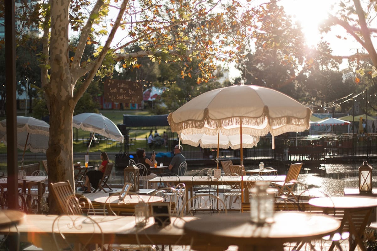 Outdoor dining by lake with umbrellas at refurbished Rymill Park Kiosk in Adelaide.