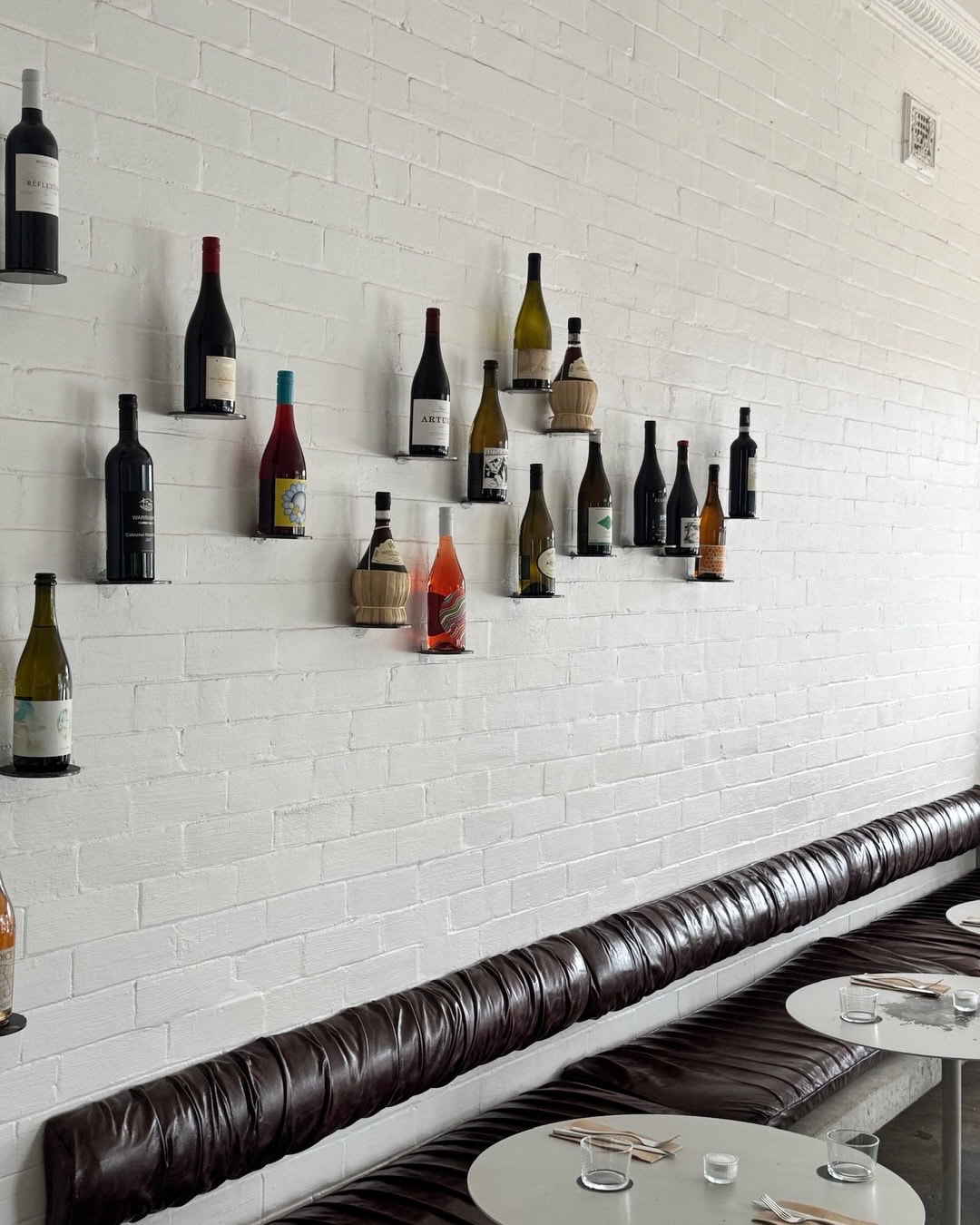 White brick wall with natural wine bottles on wall-mounted shelves above leather banquette seating at Effie's Seaforth Sydney