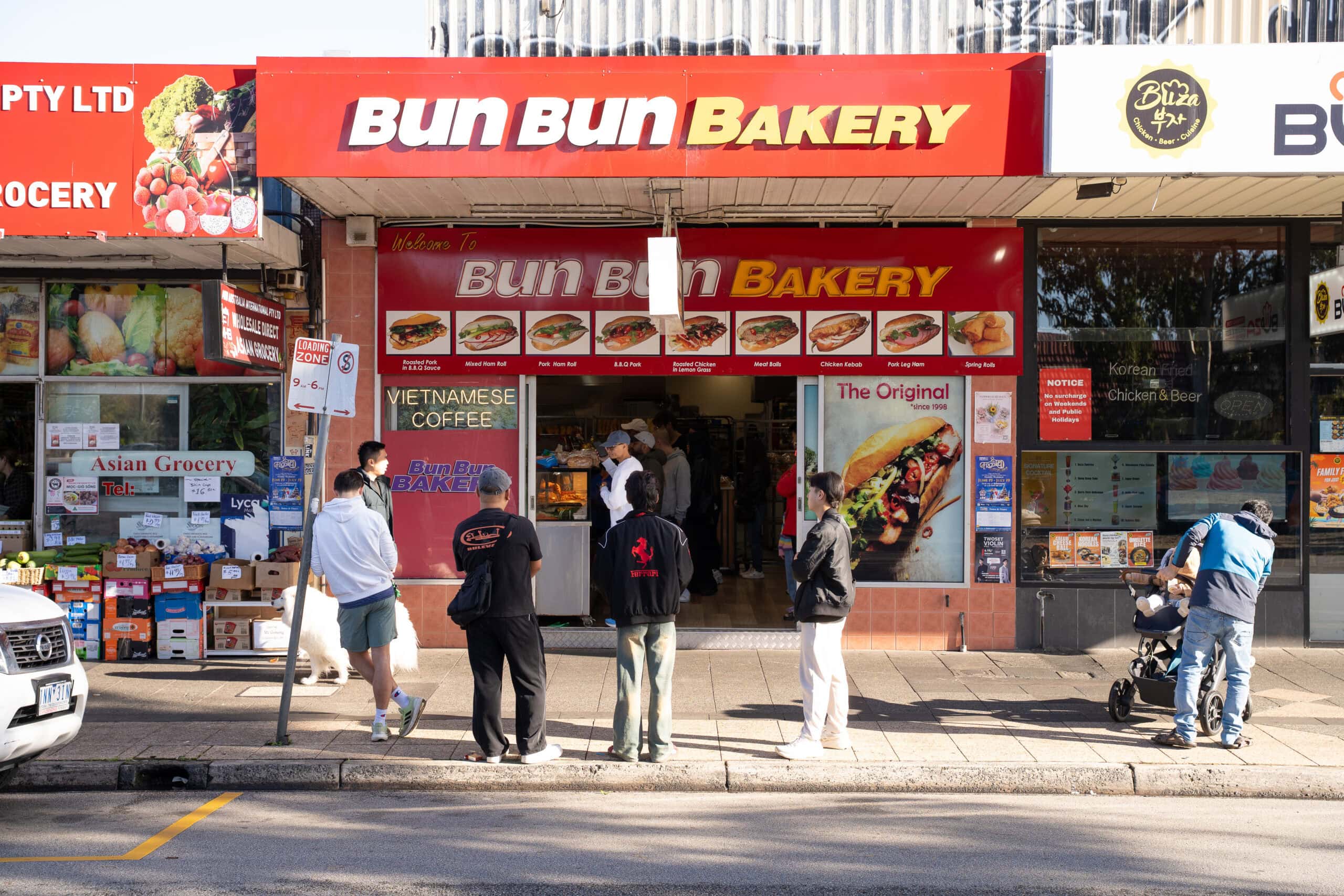 Wide street view of Bun Bun Bakery in Springvale with people gathered outside the shop.
