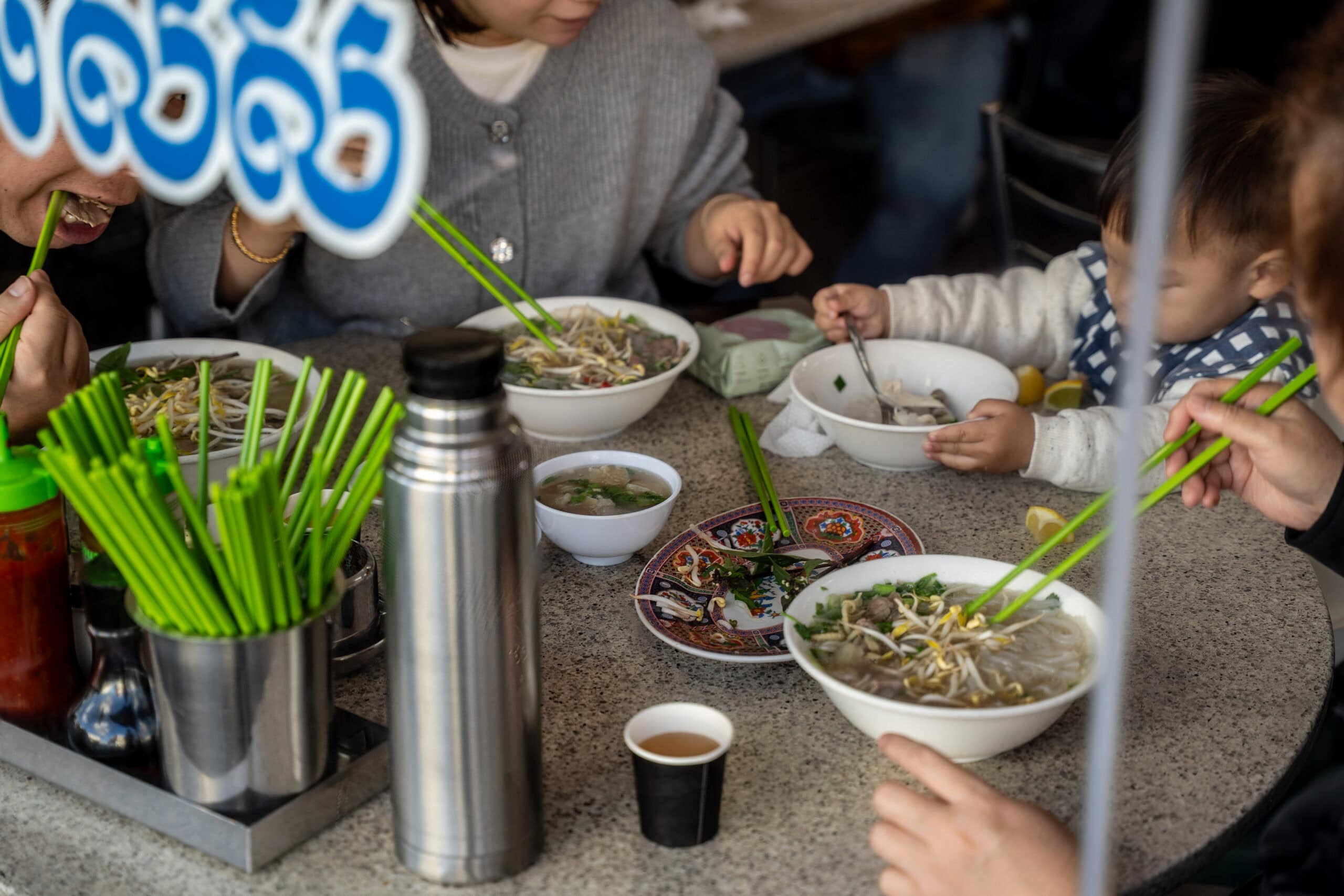 Family gathered around a table eating bowls of pho with condiments.