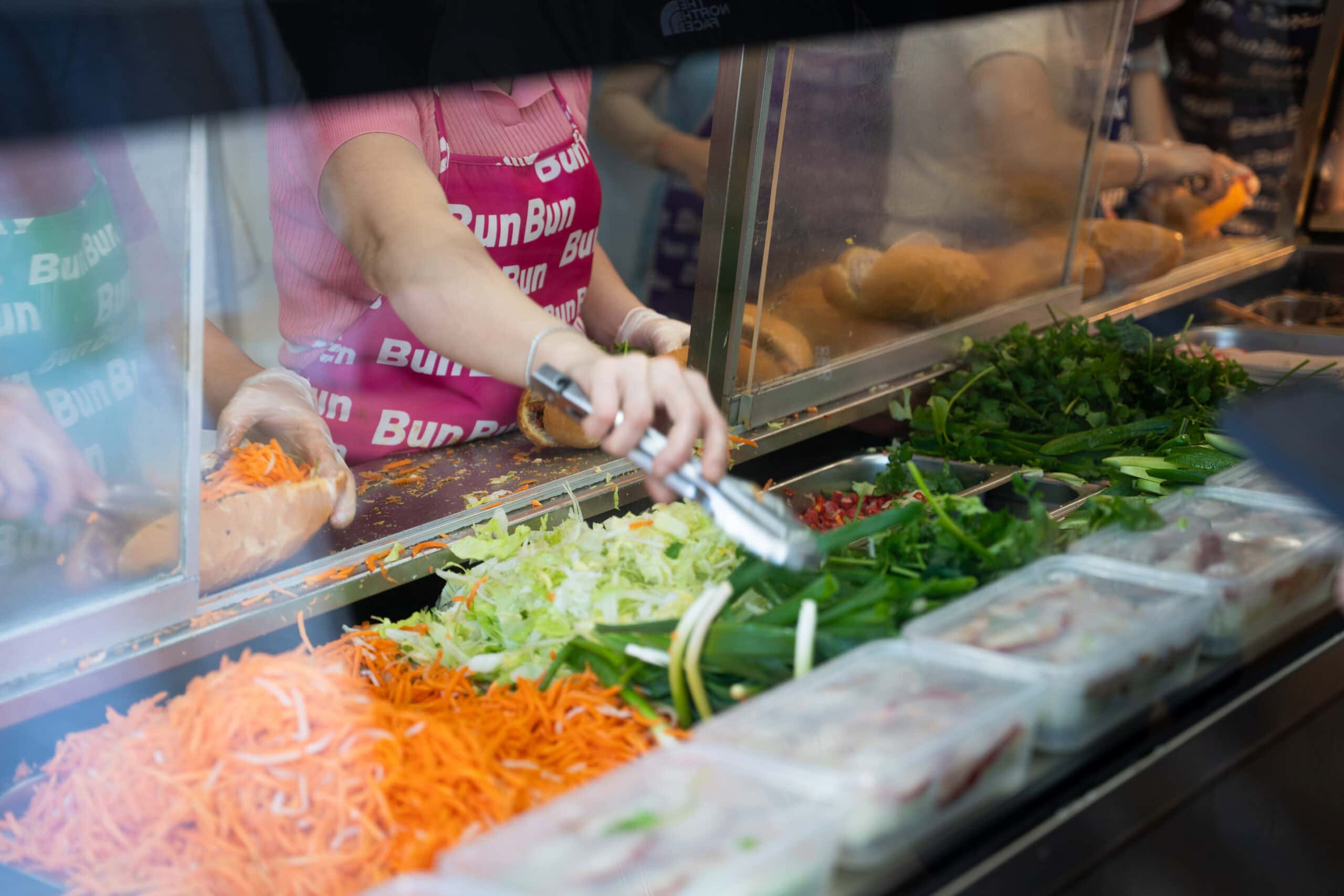 Staff assembling fresh Vietnamese banh mi with salad and herbs at Bun Bun Bakery.
