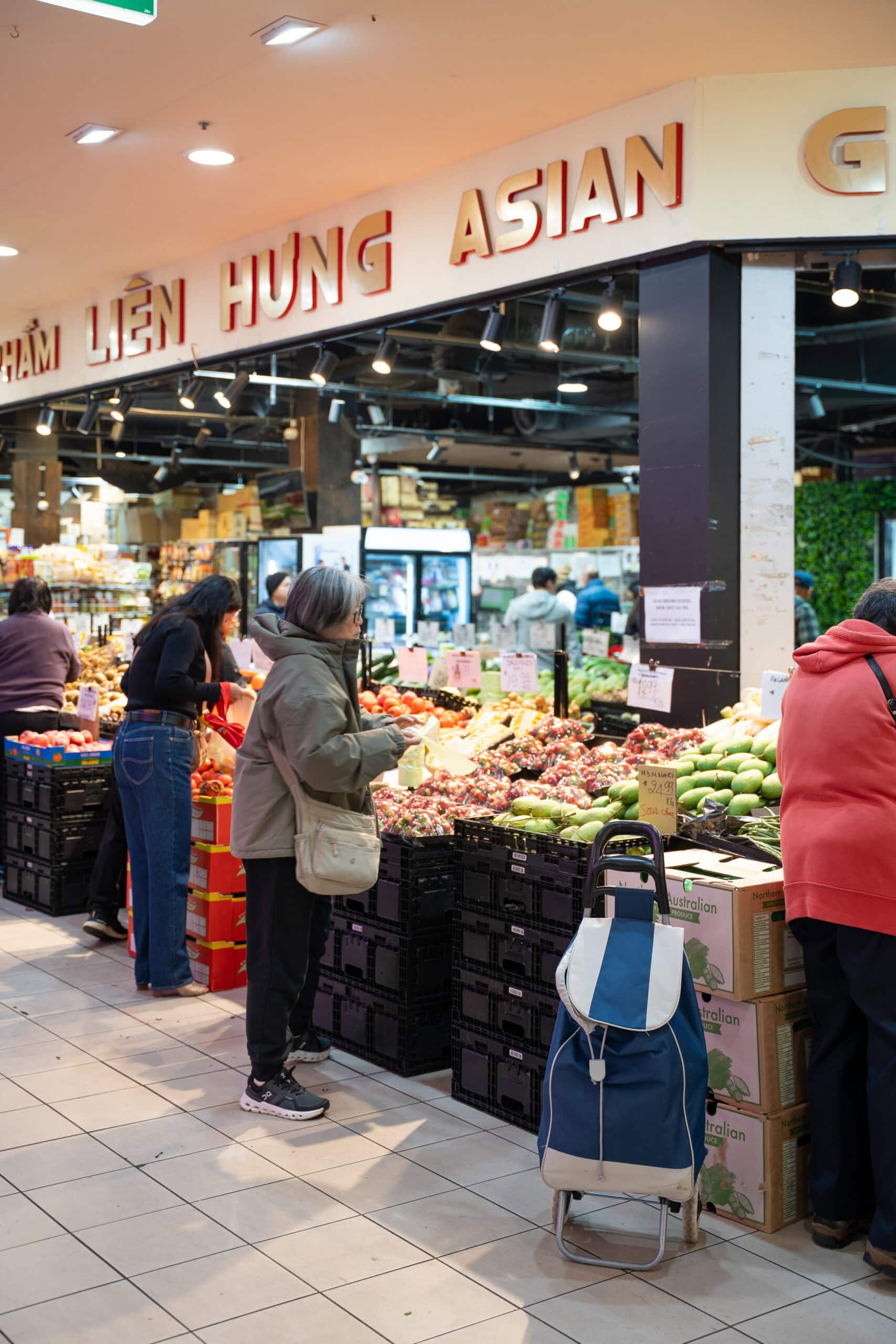 Exterior of Lien Hung Asian Grocery with customers browsing fruit and vegetable displays.