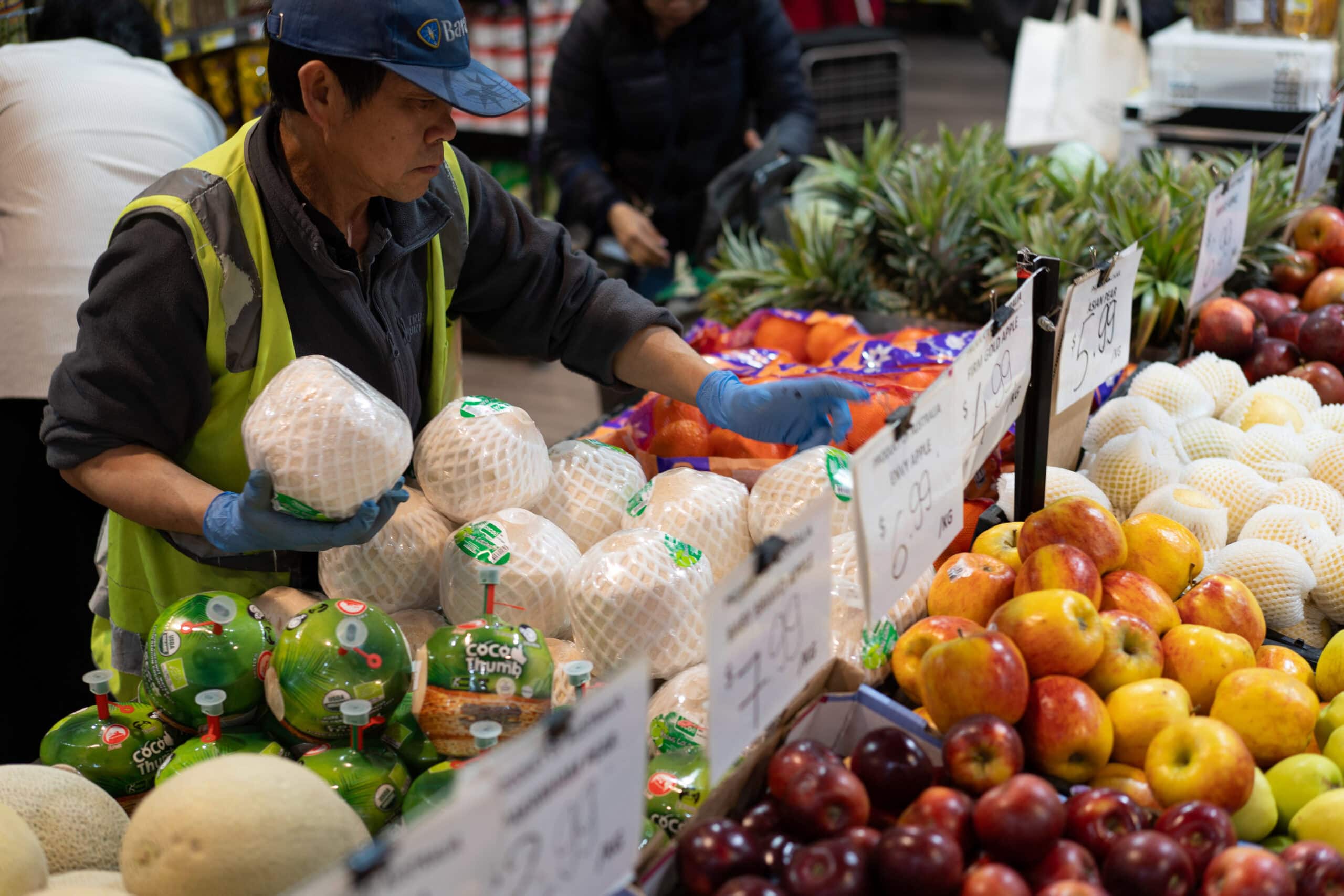 Staff member stocking fresh fruit including pomelos, apples and oranges at Lien Hung Asian Grocery.