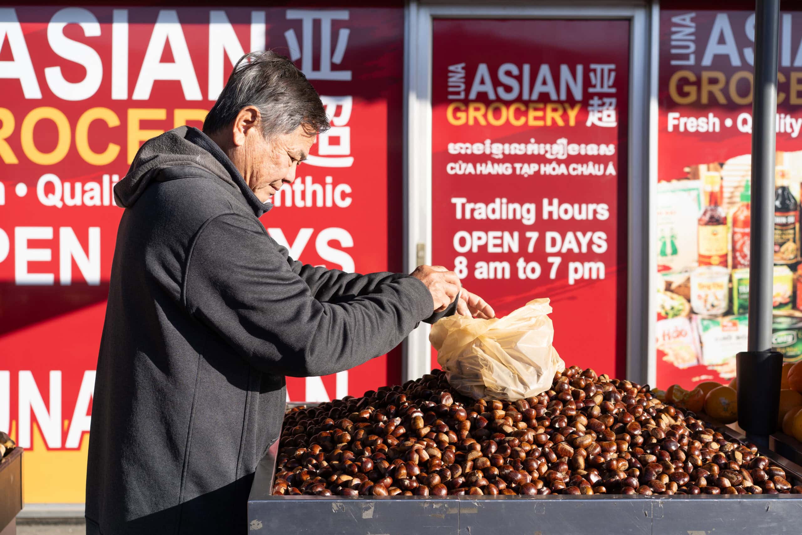 Man bagging chestnuts from a large display outside an Asian grocery.