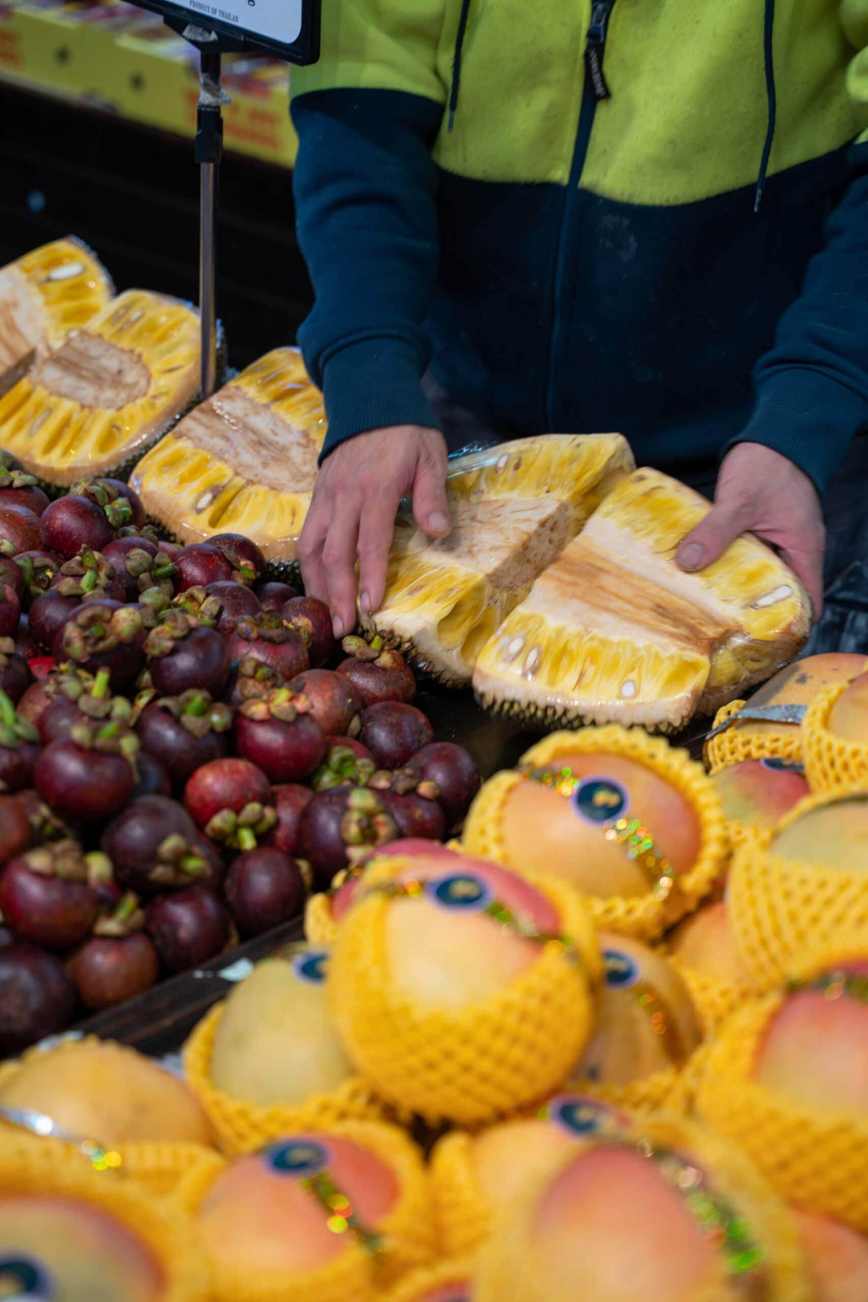 Market worker arranging fresh jackfruit beside mangosteens and mangoes.