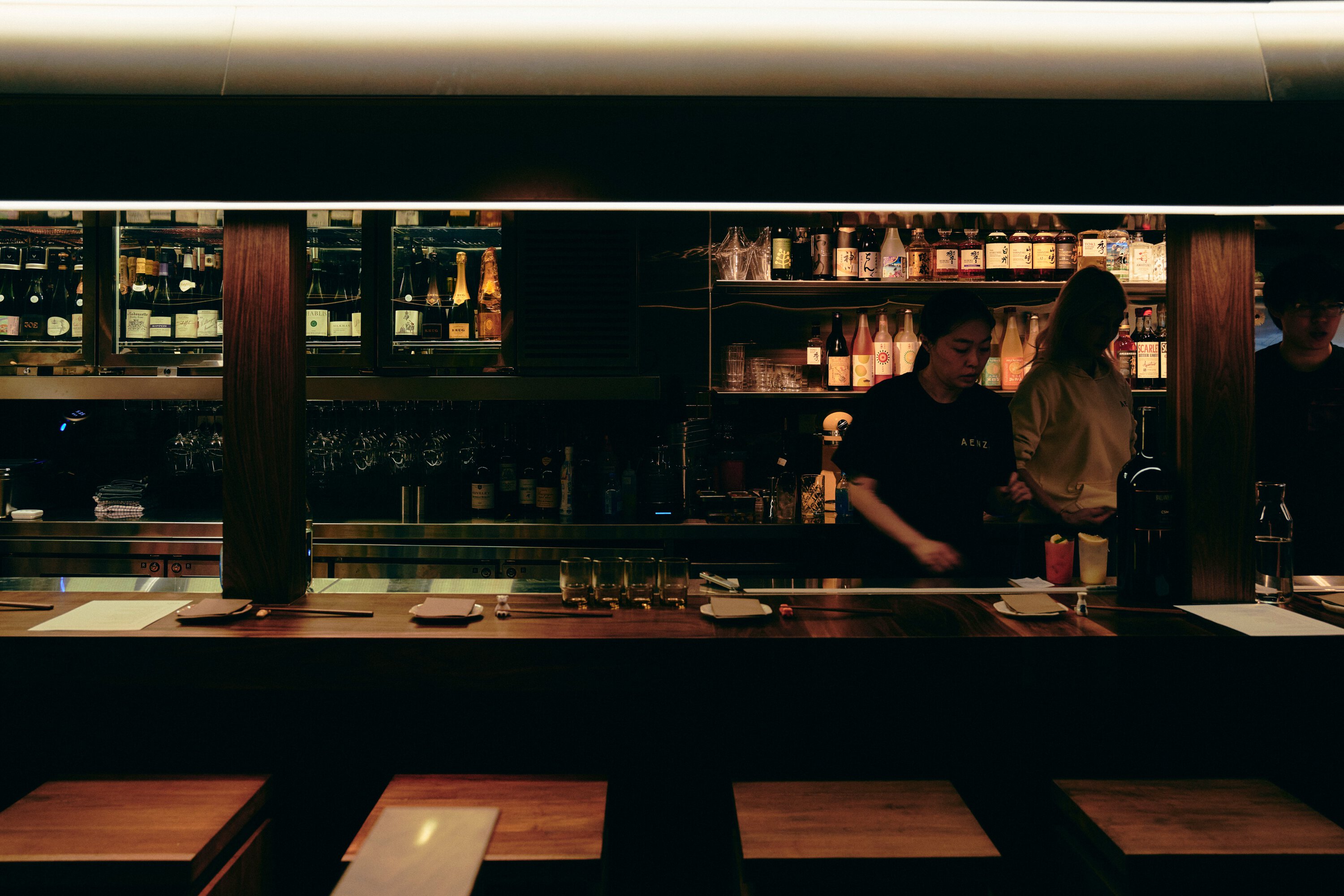 Bar staff working behind American walnut bar with sake and wine shelves at Aenza Darlinghurst Sydney