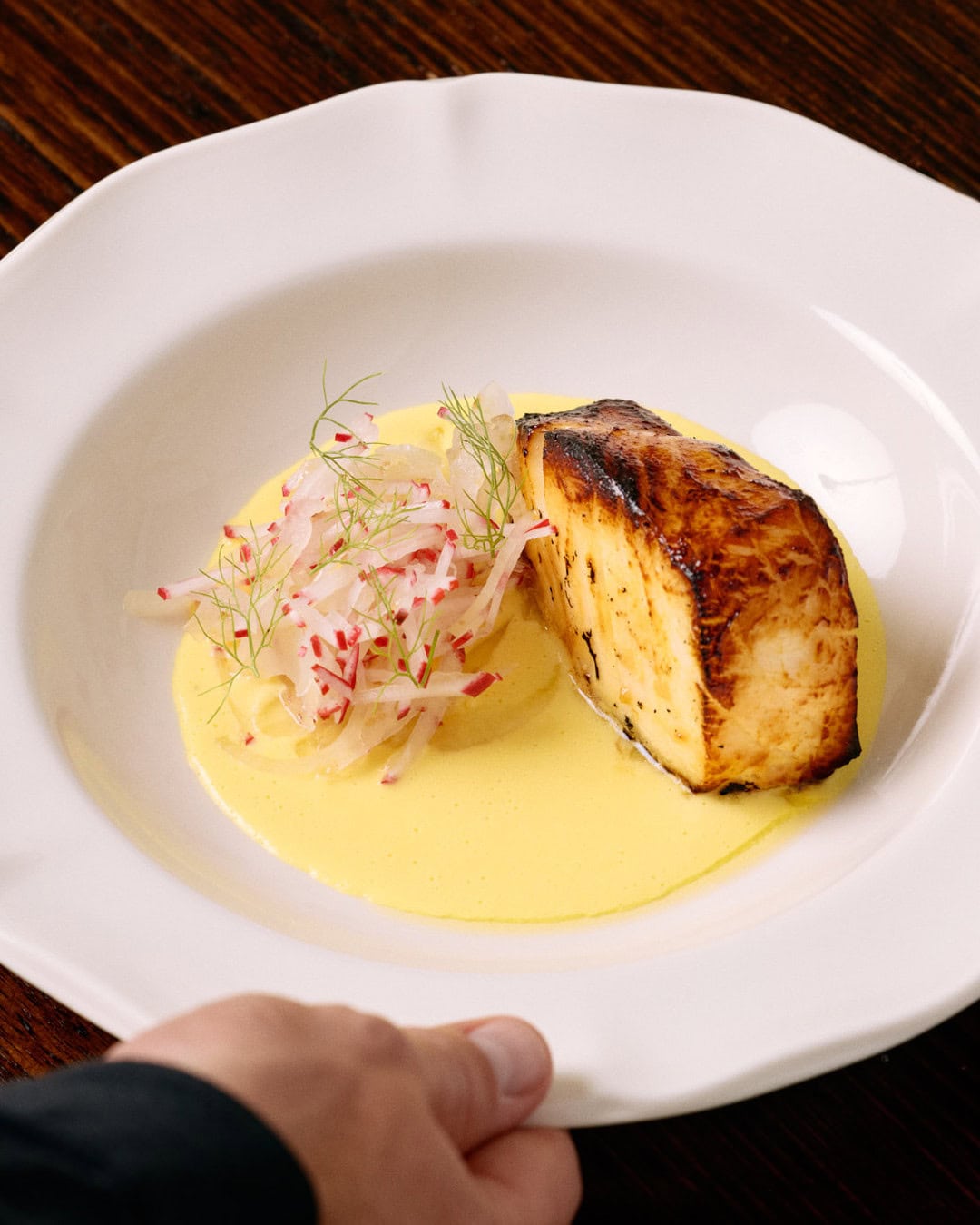 A piece of barbecued toothfish in a bowl of yellow sauce at Fosh in Brisbane.