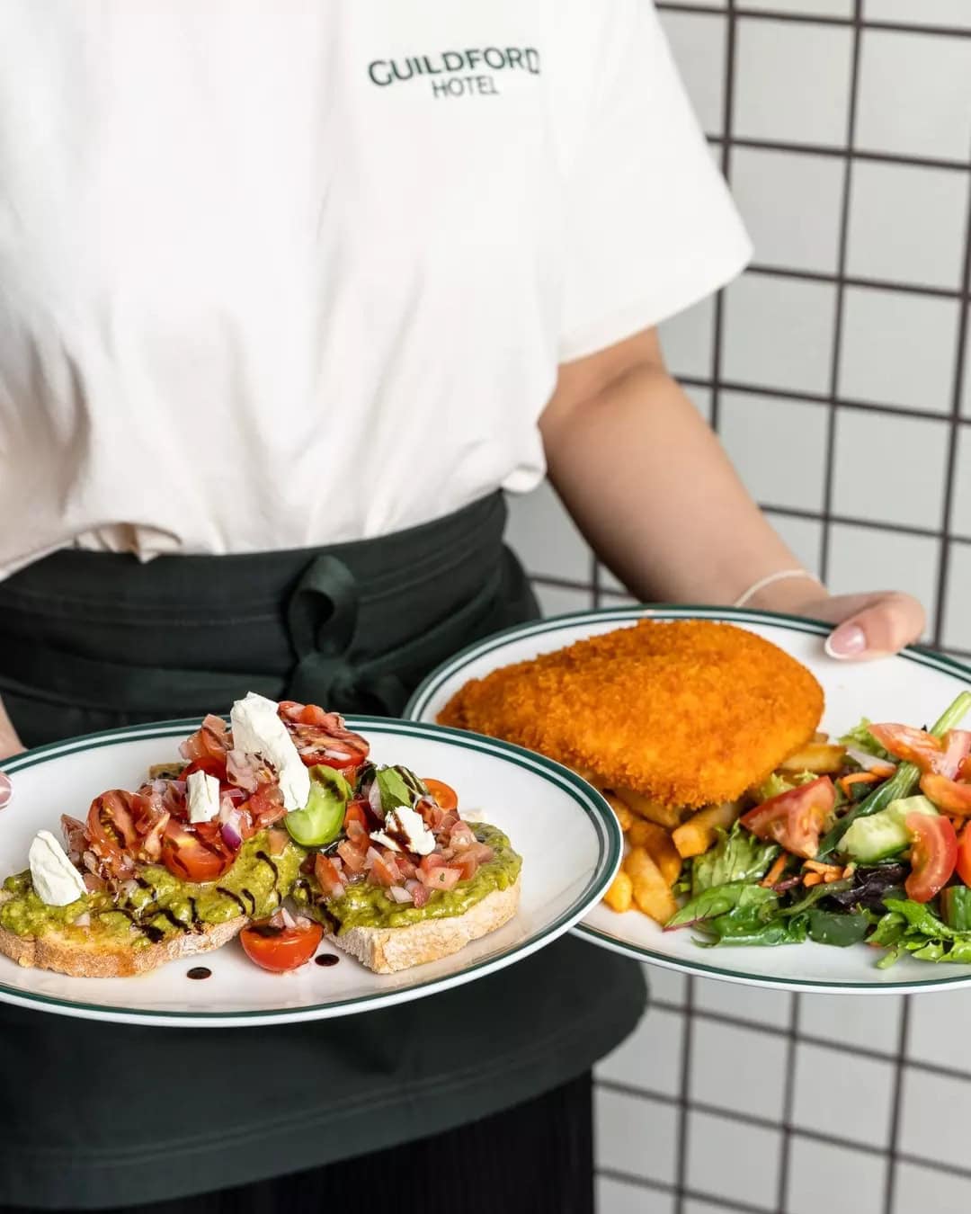 A waitress holding a plate of bruchetta and a plate of schnitzel at The Guildford Hotel.
