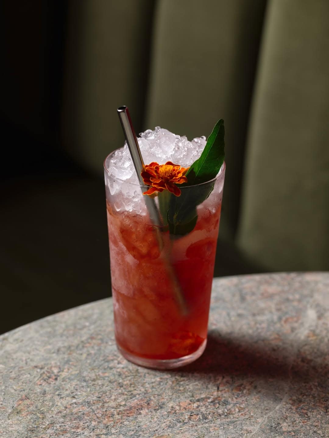 A tall cocktail sitting in front of the green velvet booth at Tailor Room in The Rocks.
