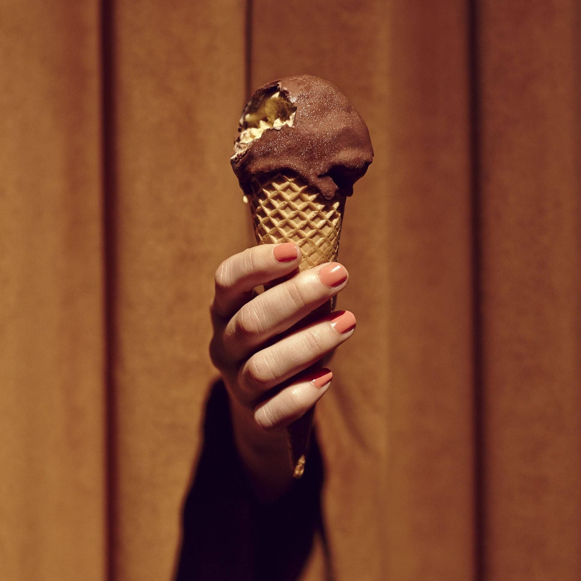 Someone with painted nails holding up a choc top ice cream with a bite taken out at Golden Age Cinema & Bar in Surry Hills.