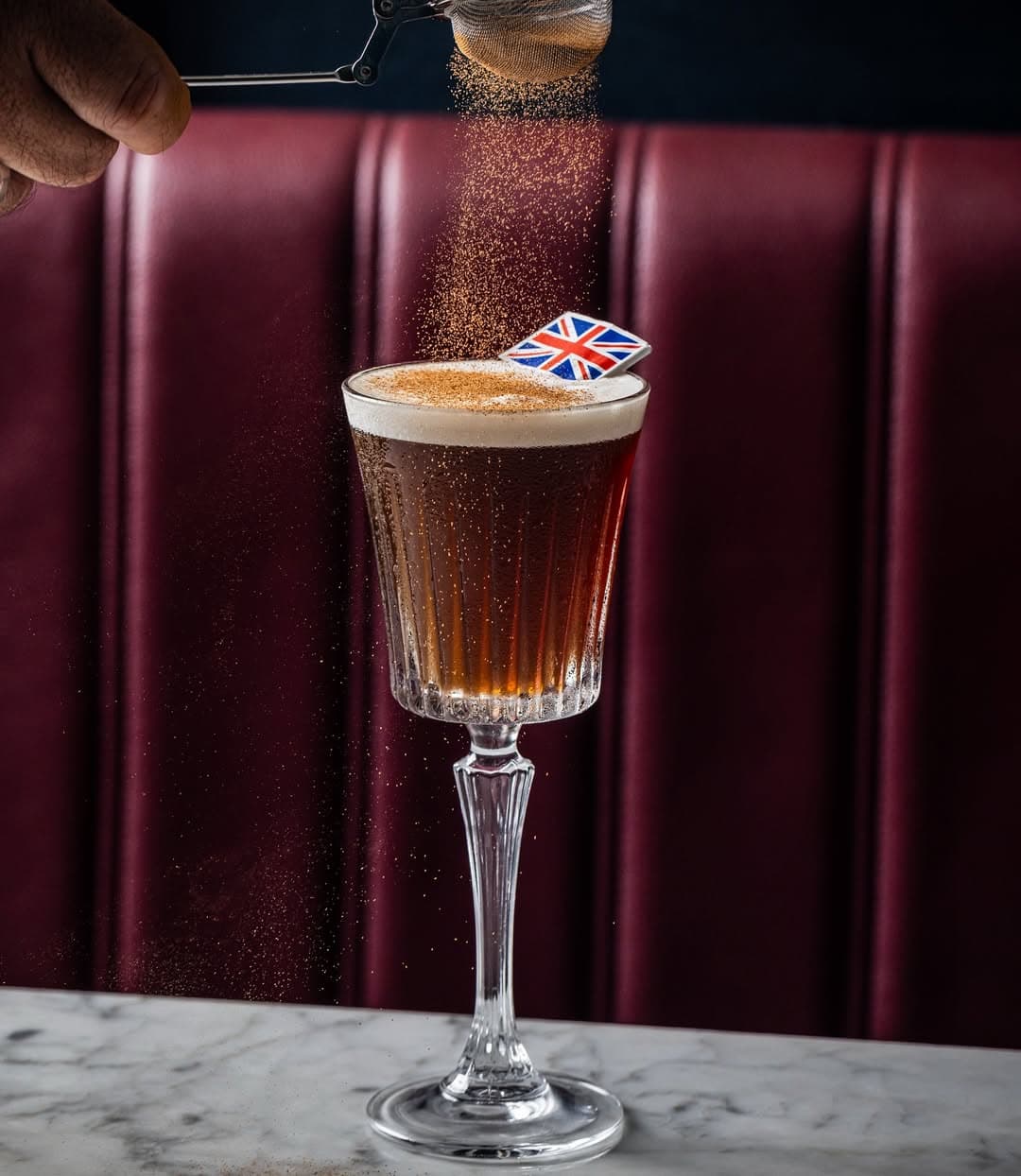 A cocktail with a British flag on it being topped with grated nutmeg at Gin Lane in Sydney.