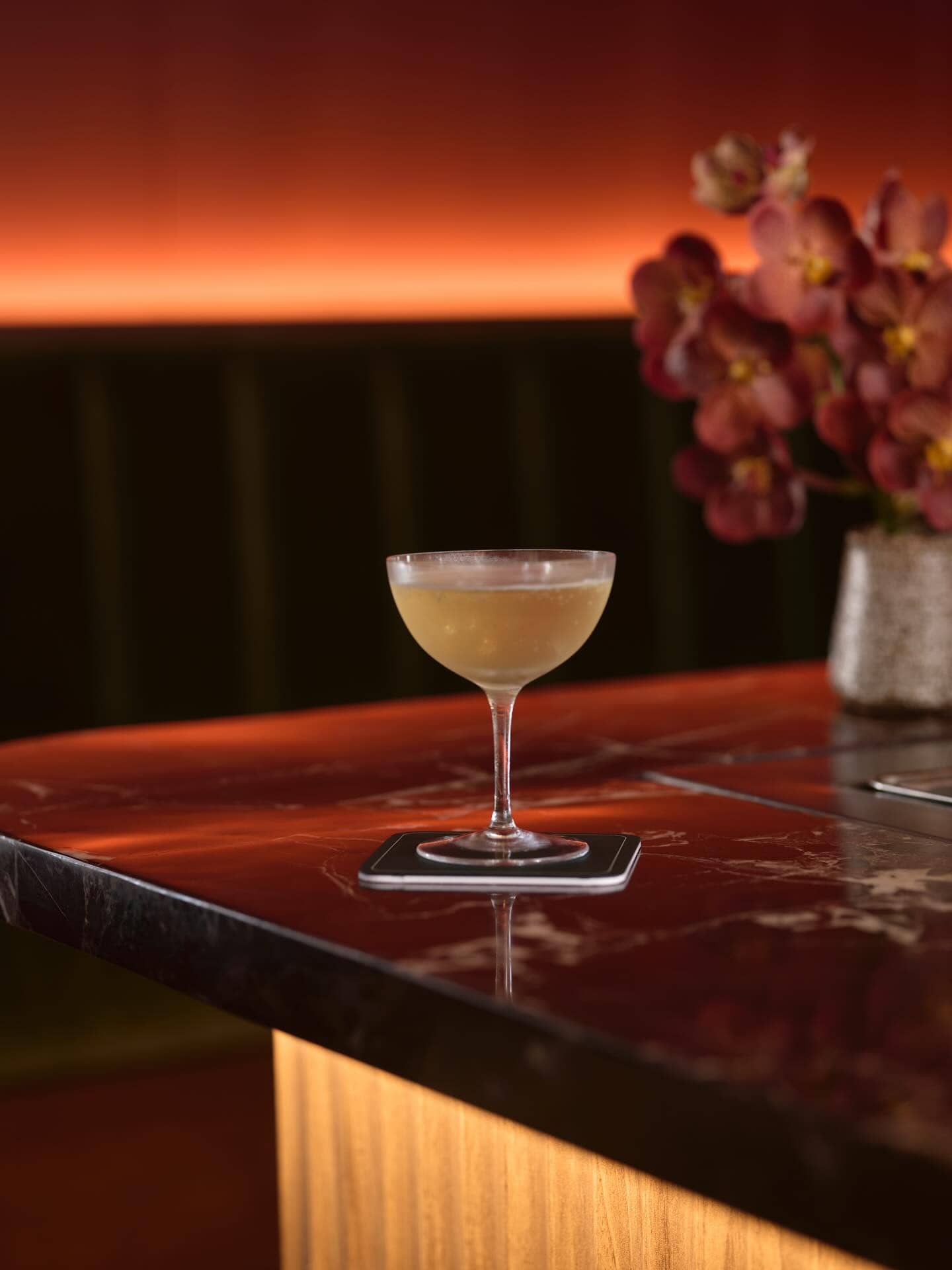 A cocktail in a coupe glass sitting atop the marble counter at Tailor Room.