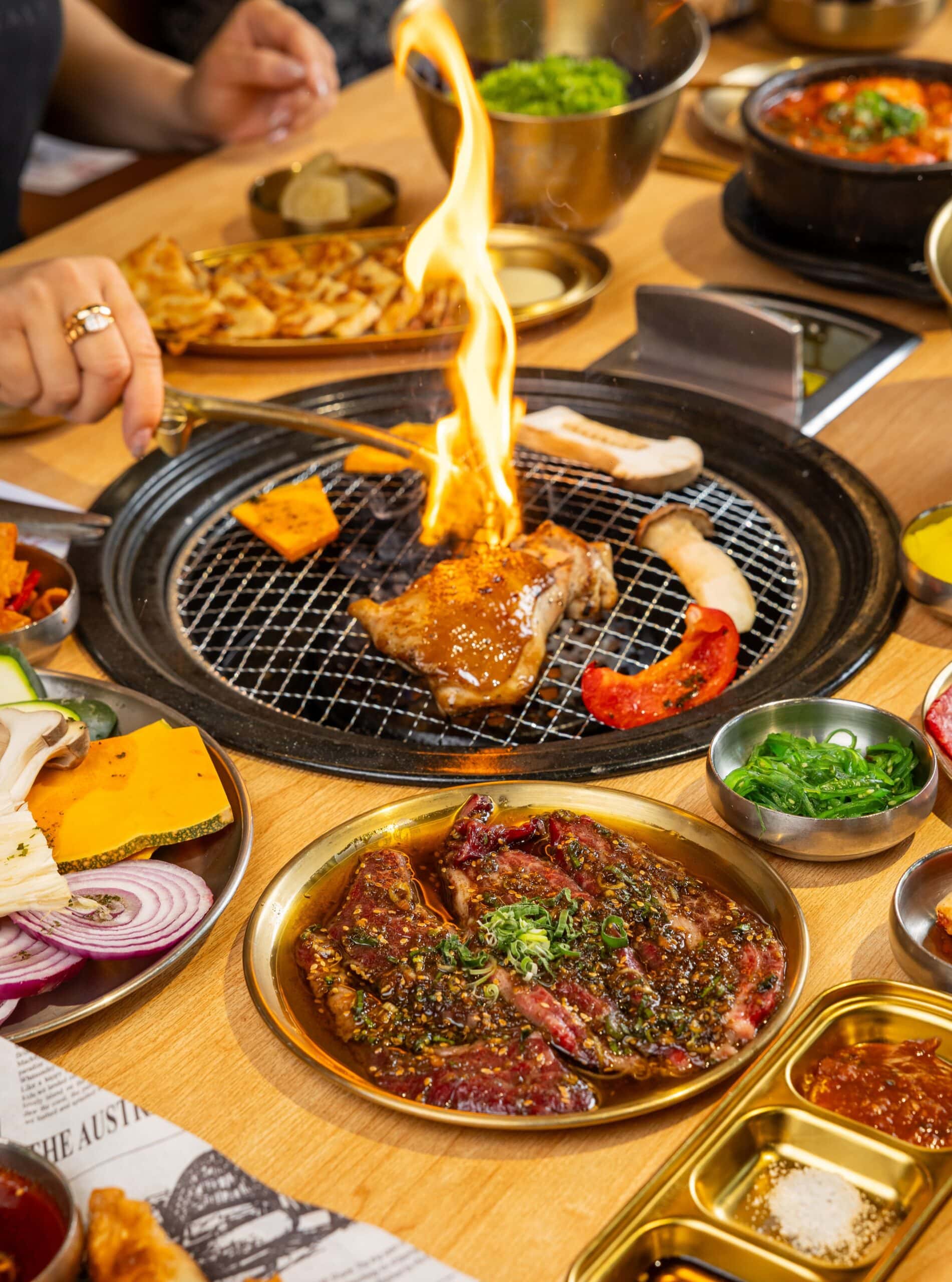 Someone at 789 Korean BBQ in Darling Square grilling a piece of meat over a flame.