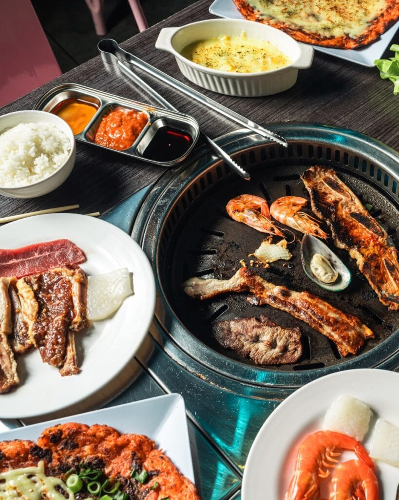 A number of plates topped with grilled meats, sitting next to a grill with pawns and meats atop at BaaOinkMoo in Liverpool.