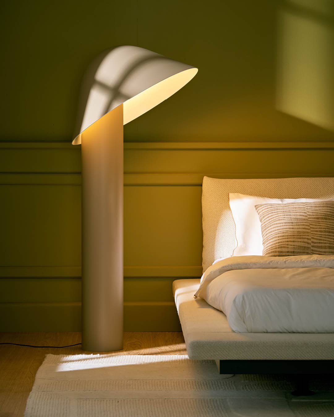 A sculptural bedside table lamp shining light onto a made bed from DOMO furniture store.