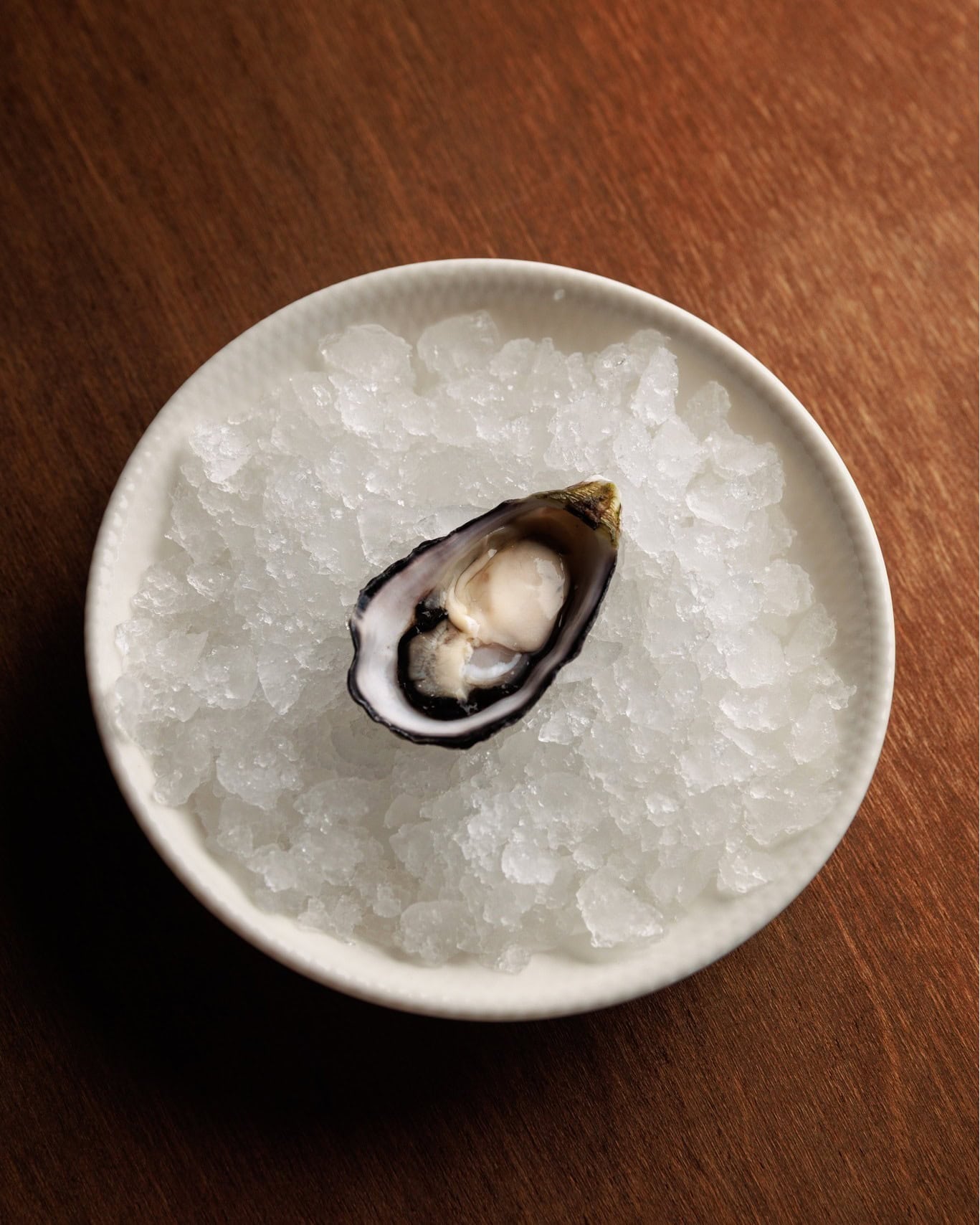 A single oyster in a bowl of ice atop a wooden table at Tillerman Restaurant in Brisbane.