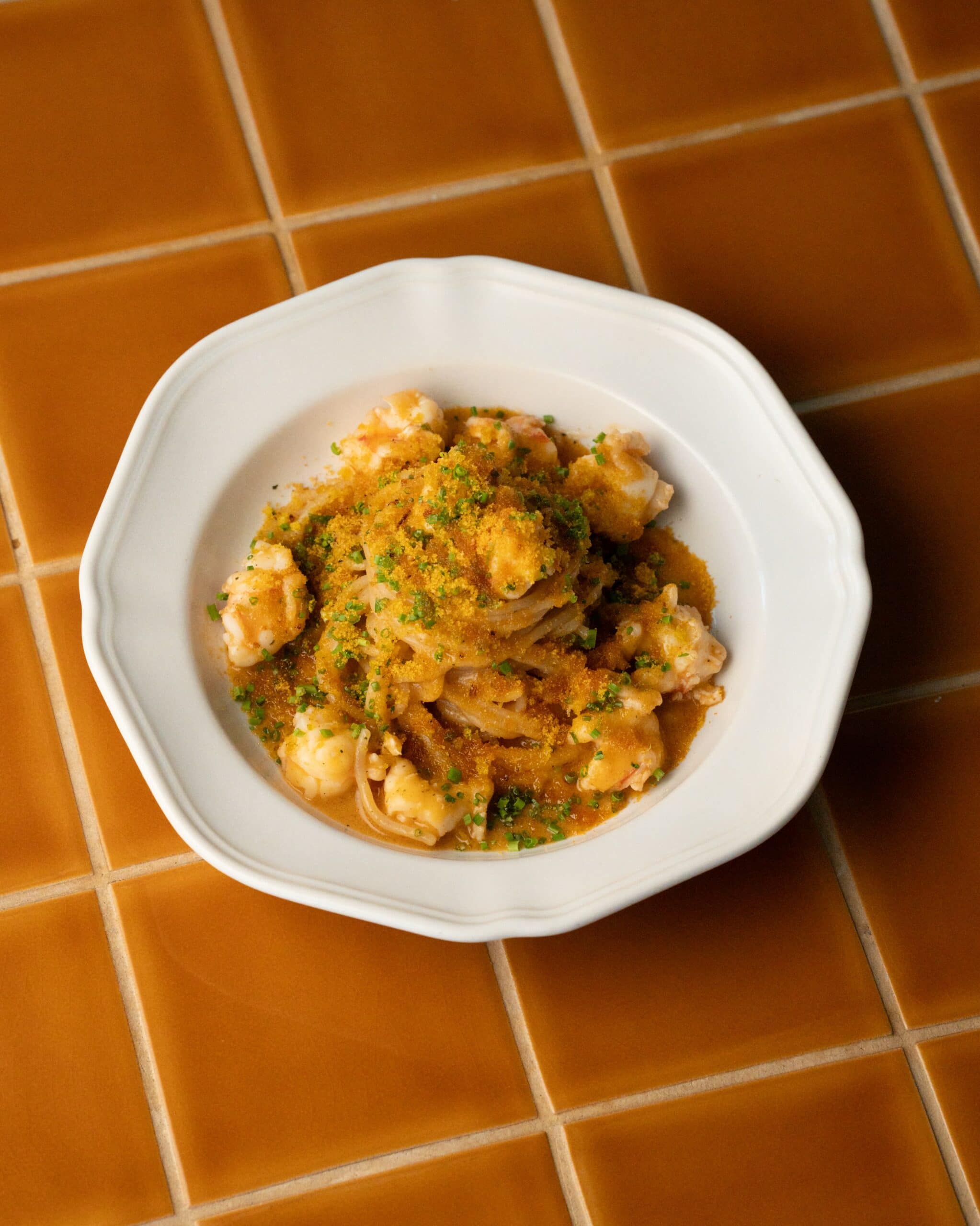 A bowl of prawn pasta from Gina Pasta Bar in Barangaroo sitting atop a burnt orange-tiled table top.
