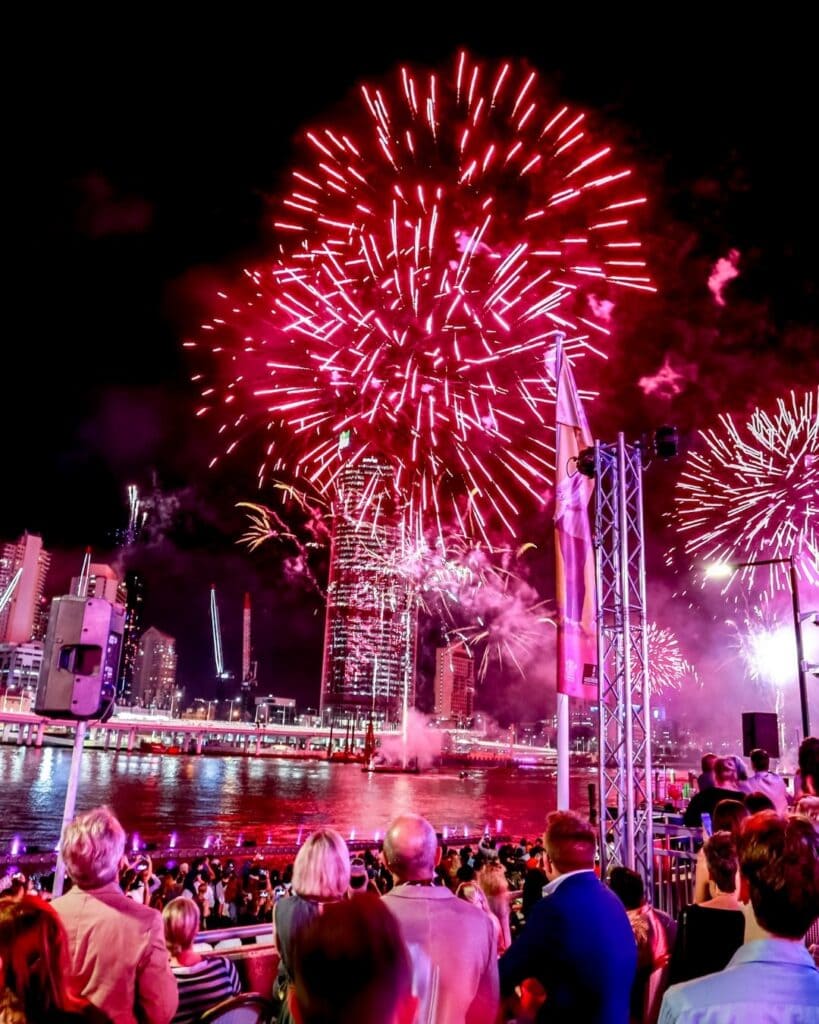 People watching on as bright red fireworks explode as part of Riverfire.