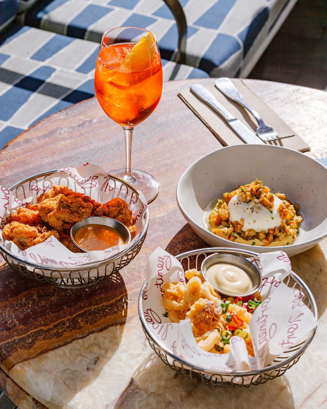 Three plates of snacks and an Aperol spritz atop a table at Martinez in Sydney.