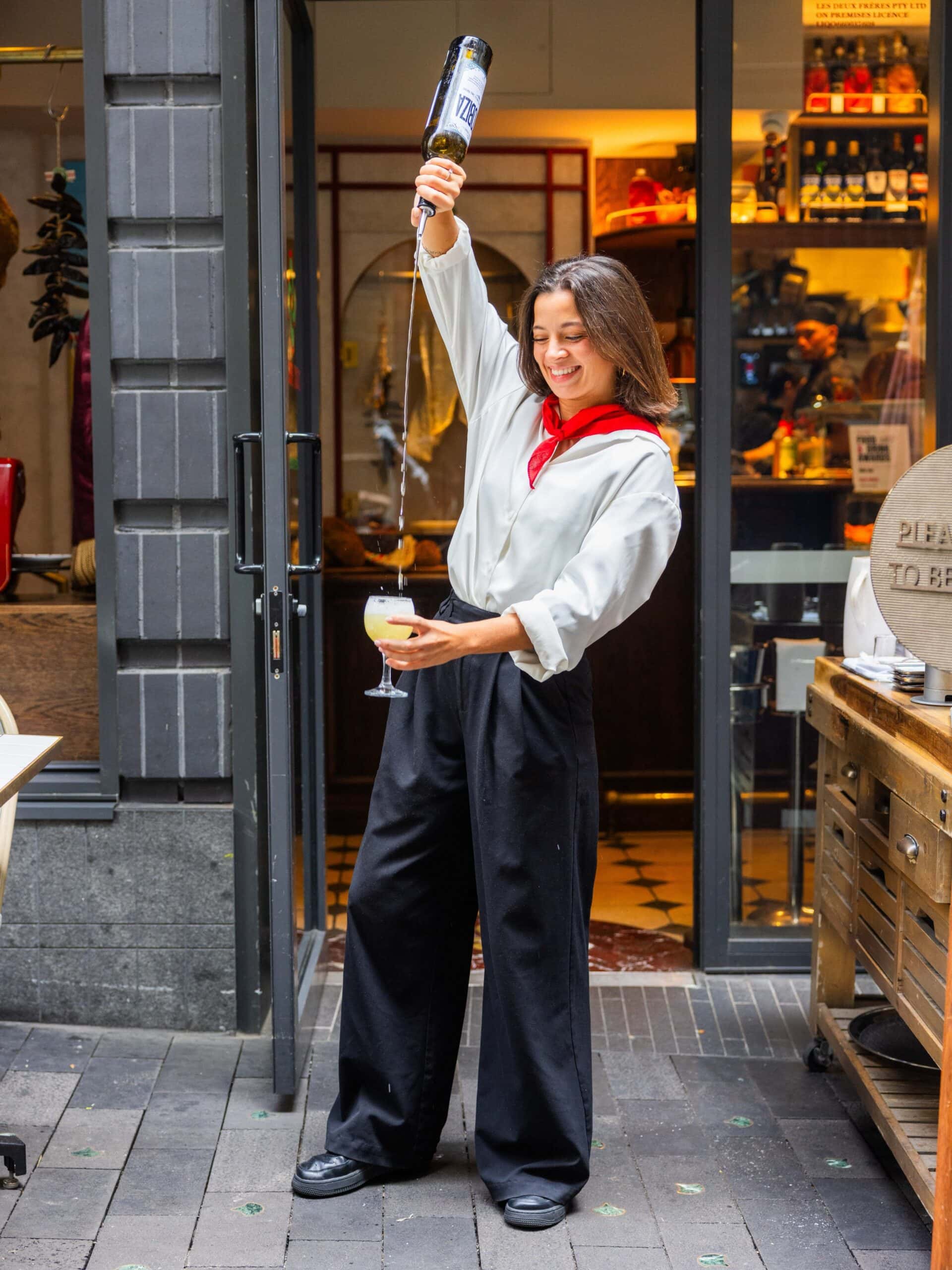 A waitress with a red bandana around her neck pouring a cocktail at Deux Feres in Circular Quay.