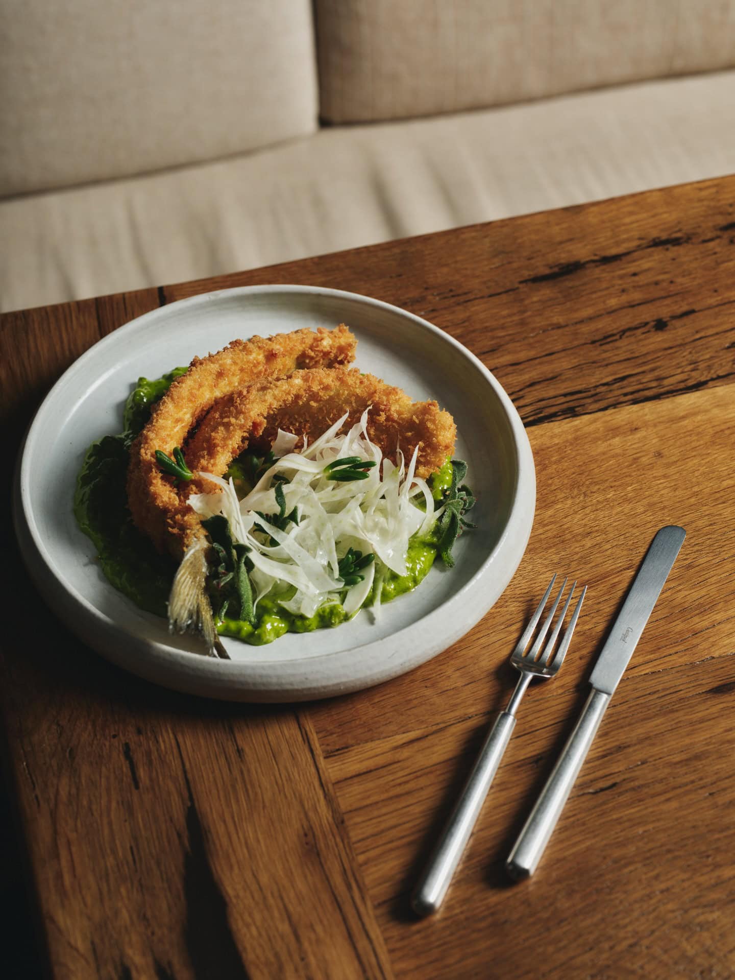 A plate of crumbed whiting salad on the edge of a wooden table at White Horse in Surry Hills.