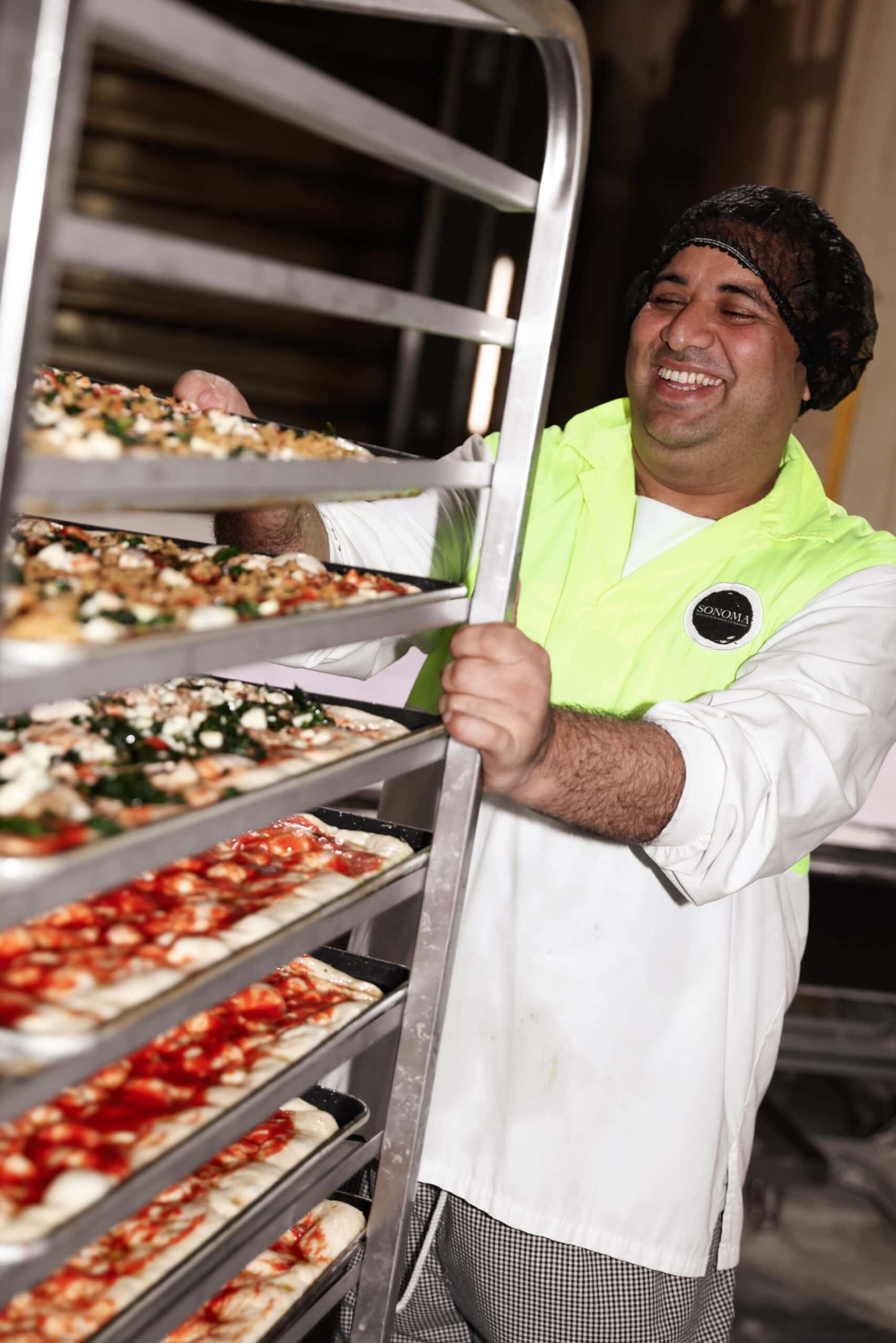 Sonoma baker smiling while loading trays of pizza dough at the Alexandria bakery, Sydney