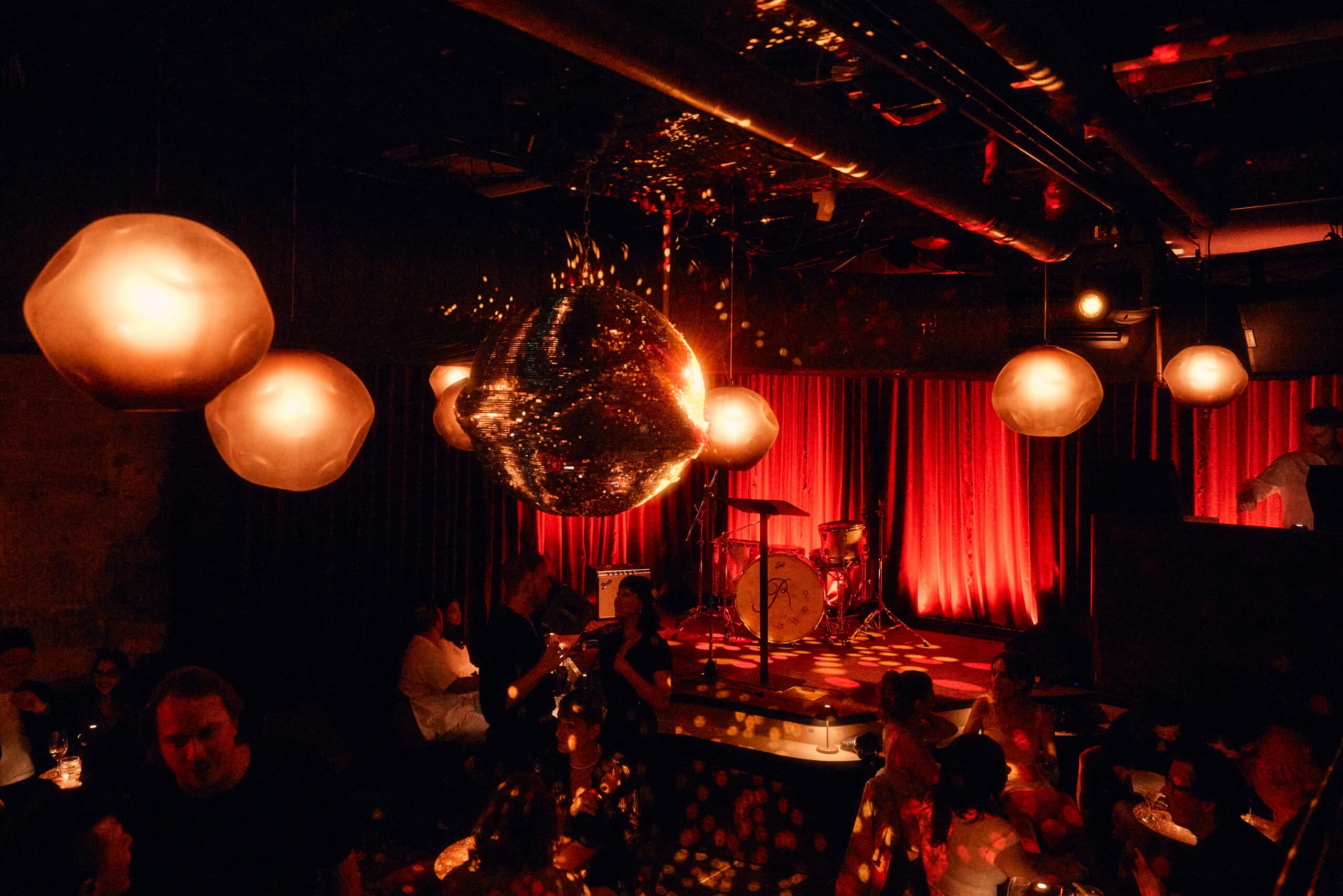 Mirror ball and glowing pendant lights above the sunken dance floor and red-curtained stage at Razz Room daiquiri bar, Sydney CBD