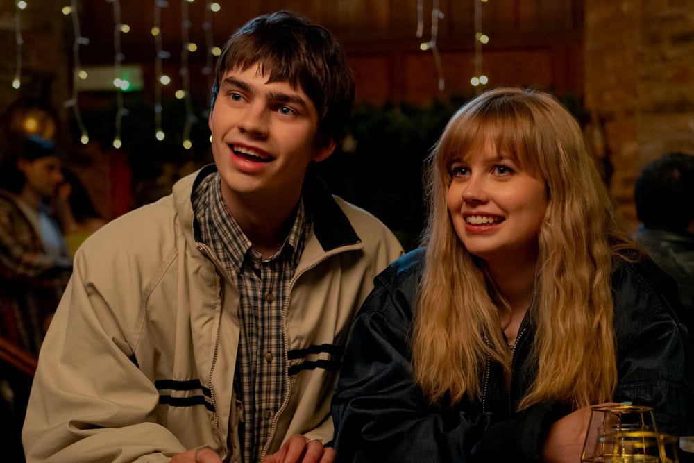 Angourie Rice and a co-star smiling in a candlelit scene from the romantic comedy Finding Emily