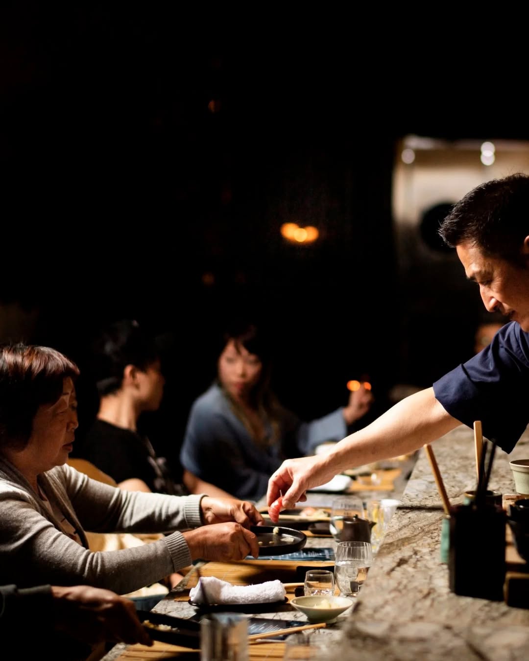 An omakase chef handing a diner a plate at Ora in Sydney.