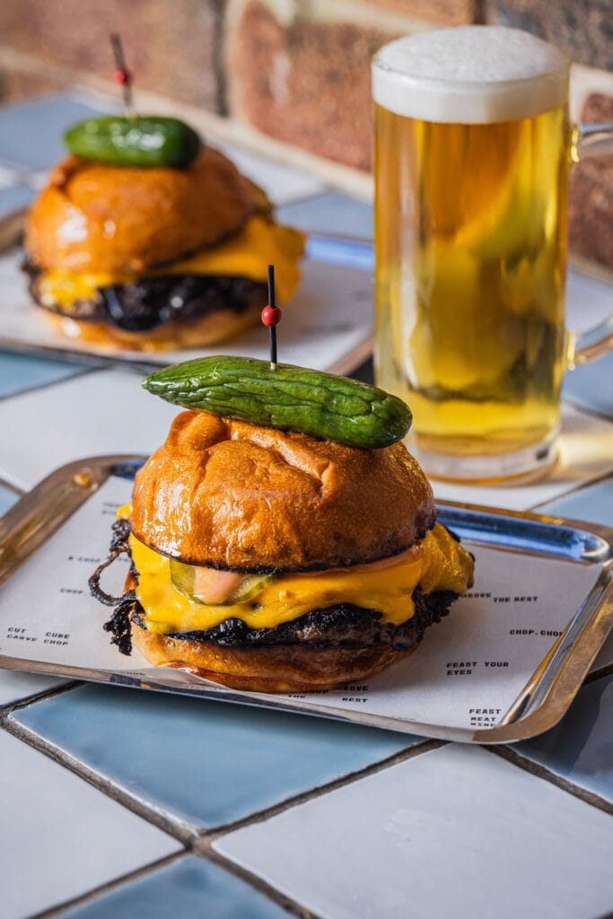 Smash burger with melted cheese and pickle alongside a beer at Chophouse, Sydney CBD