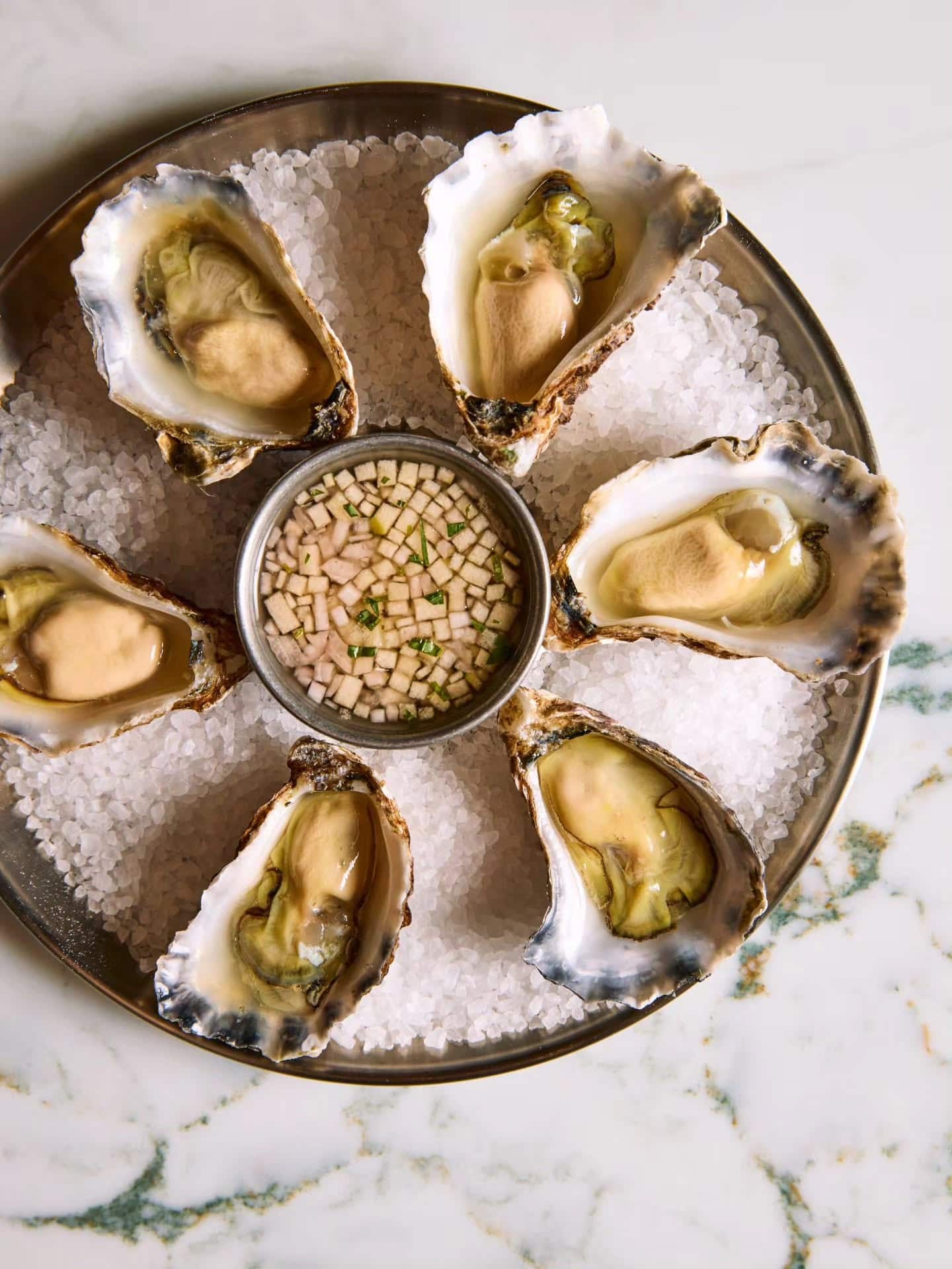 Appellation oysters served on a tray of decorative salt on a marbled table.