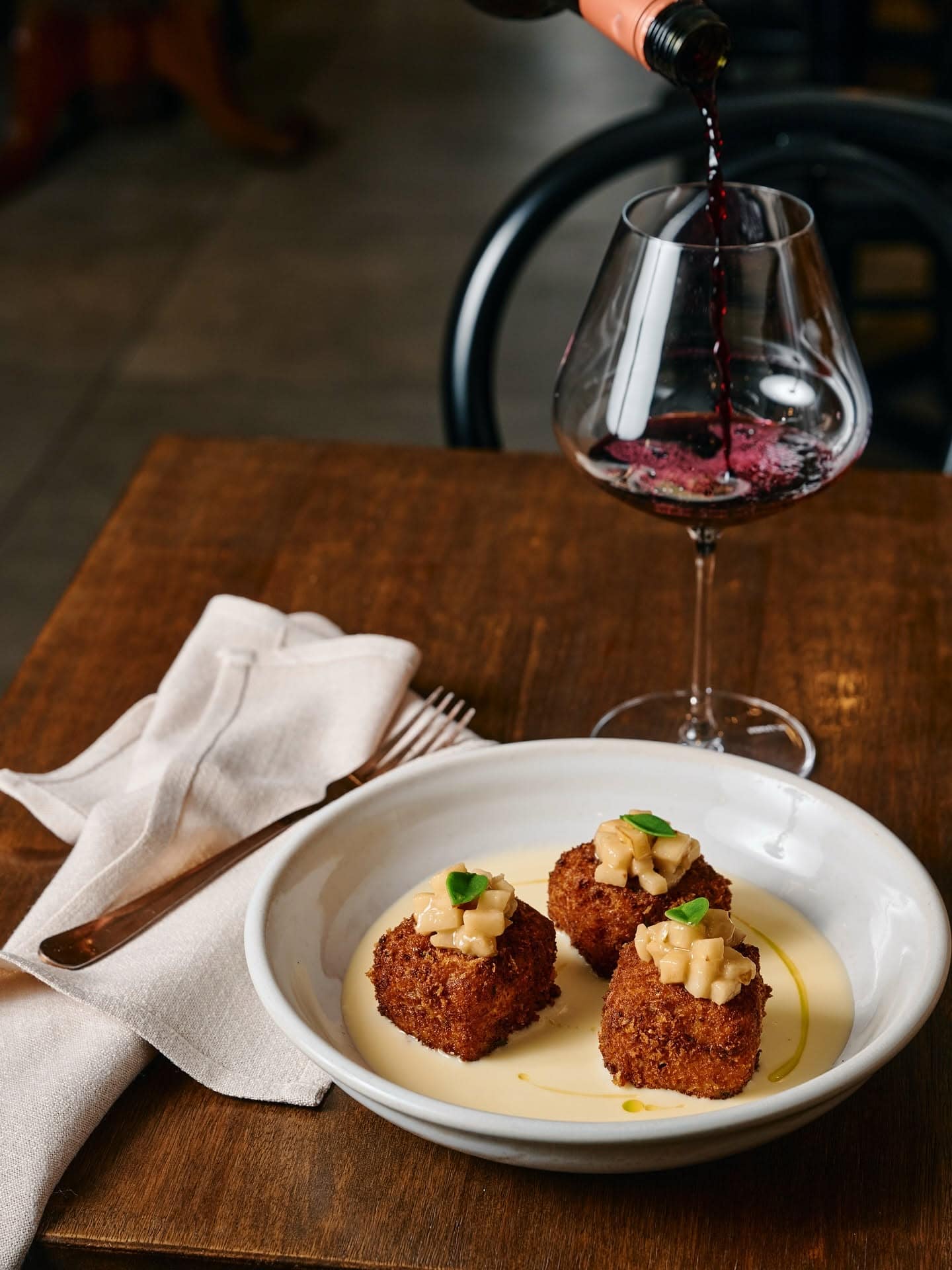 Crisp croquettes with creamy sauce served alongside red wine at Buono Restaurant & Bar in Parkdale, Melbourne.