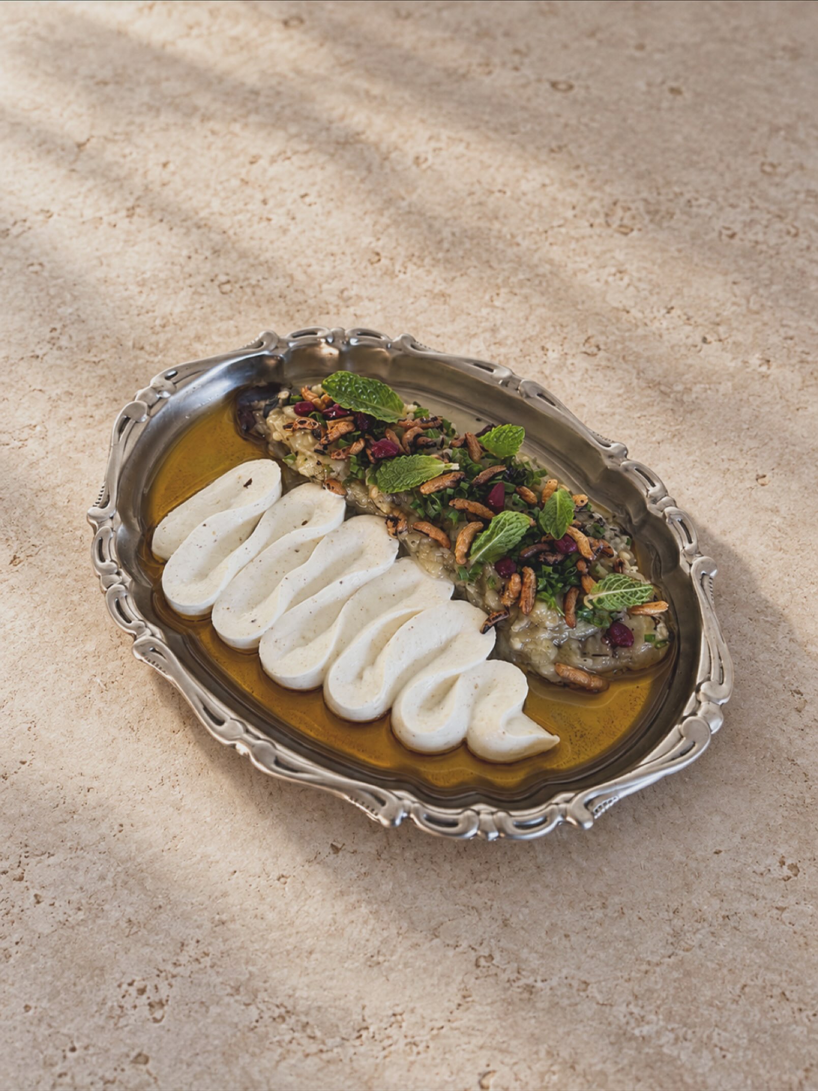 Charred and marinated eggplant served with burnt butter on a silver platter.