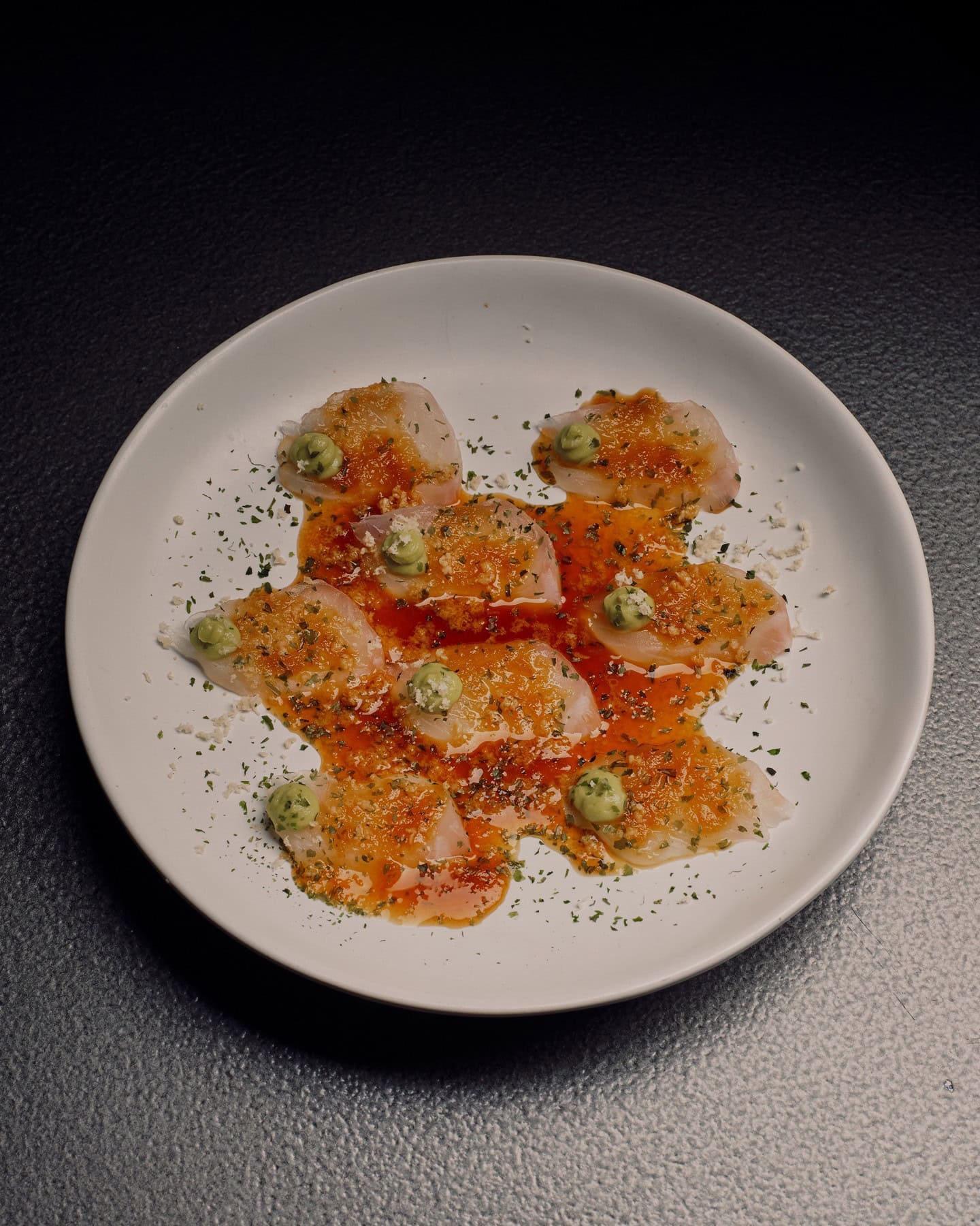 A white plate with ceviche dressed with an orange sauce.