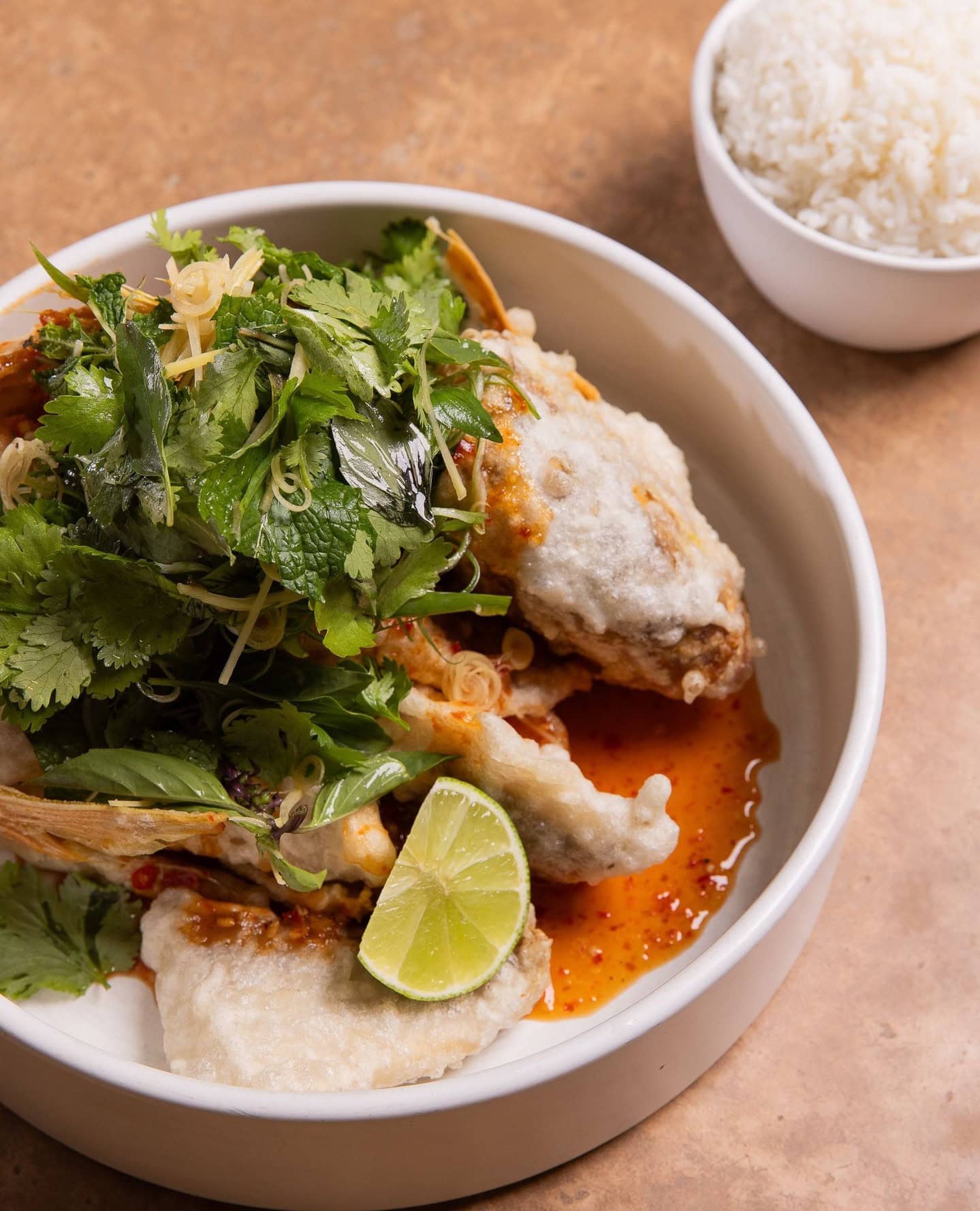 A bowl of crispy fried fish in a four chilli dressing, served with fresh lime, rice and lots of fresh herbs on top.