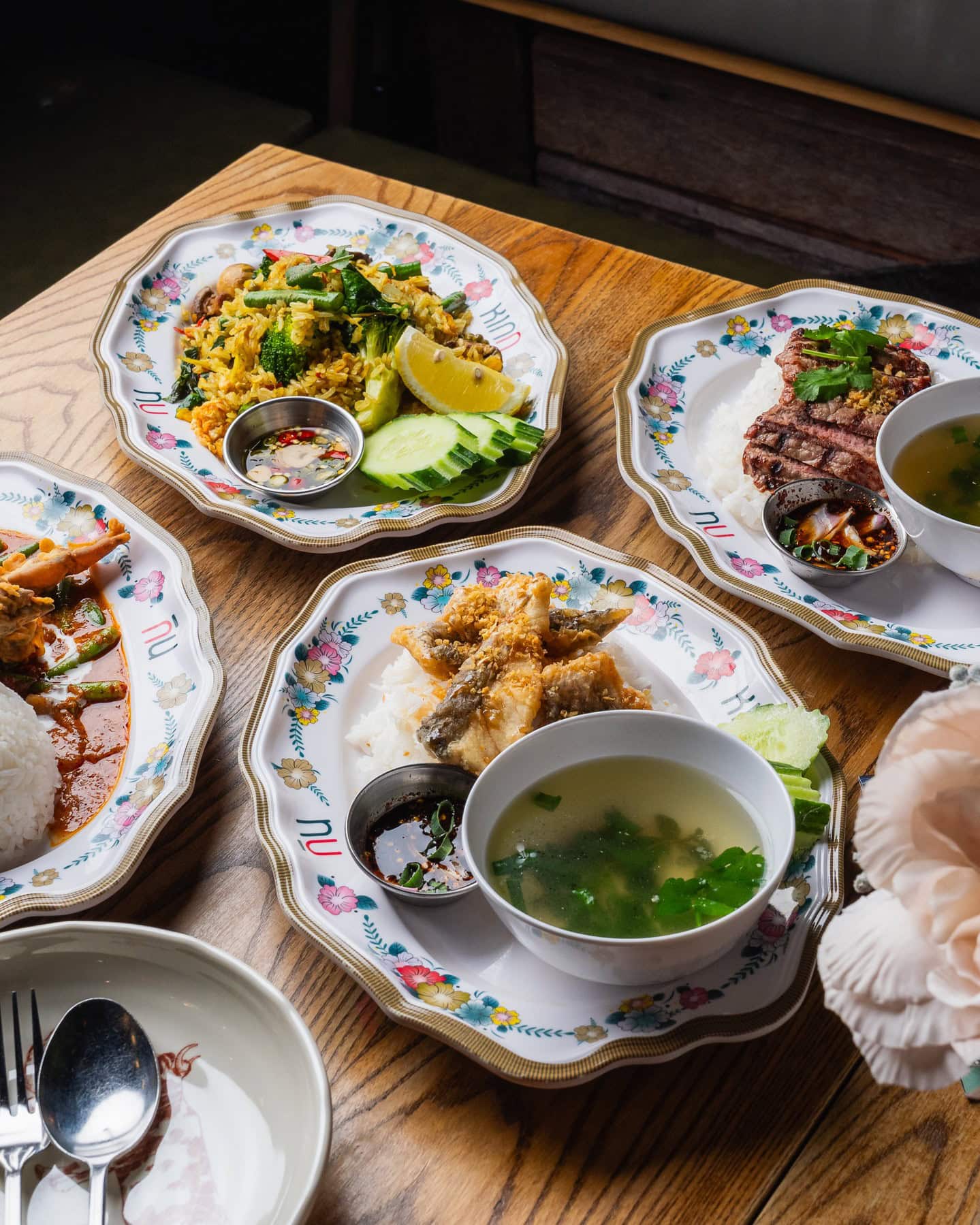 A brown table bearing four colourful share plates of meat fish rice and curry.