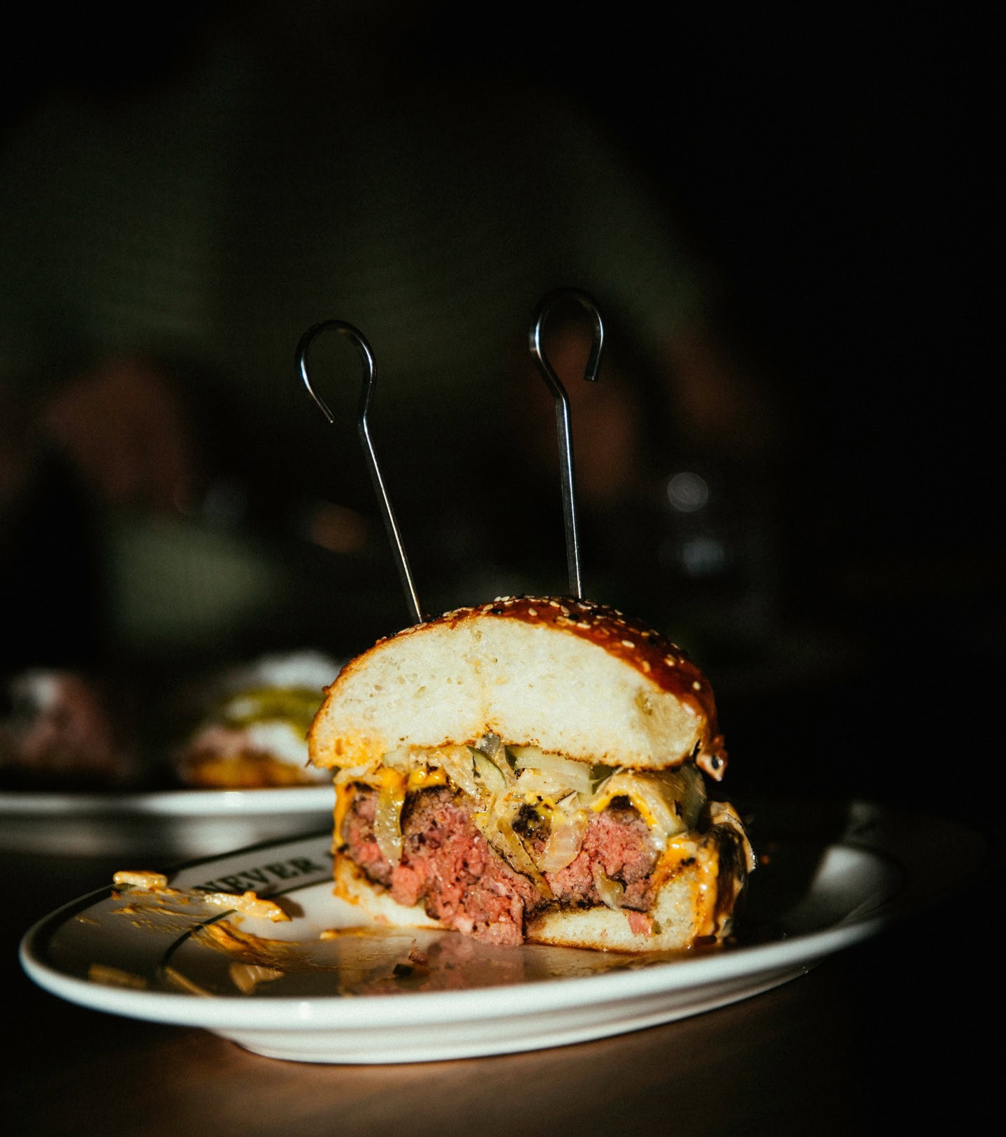 A cheeseburger cut in half on a white serving platter, showing medium rare beef patty, pickles and mustard.