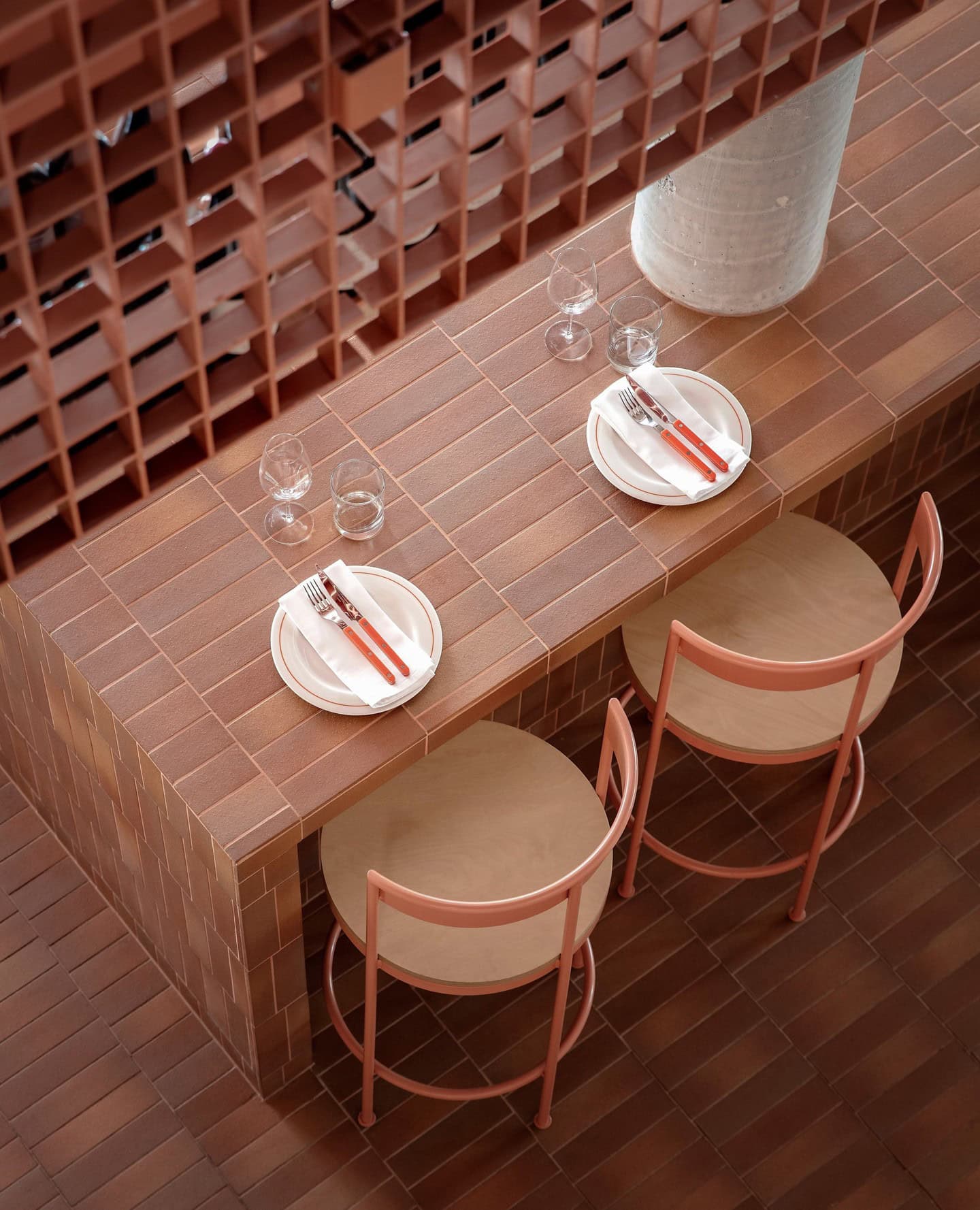 A top-down shot of an Italian restaurant, showing a terracotta tile table and floor, set with blush pink chairs.