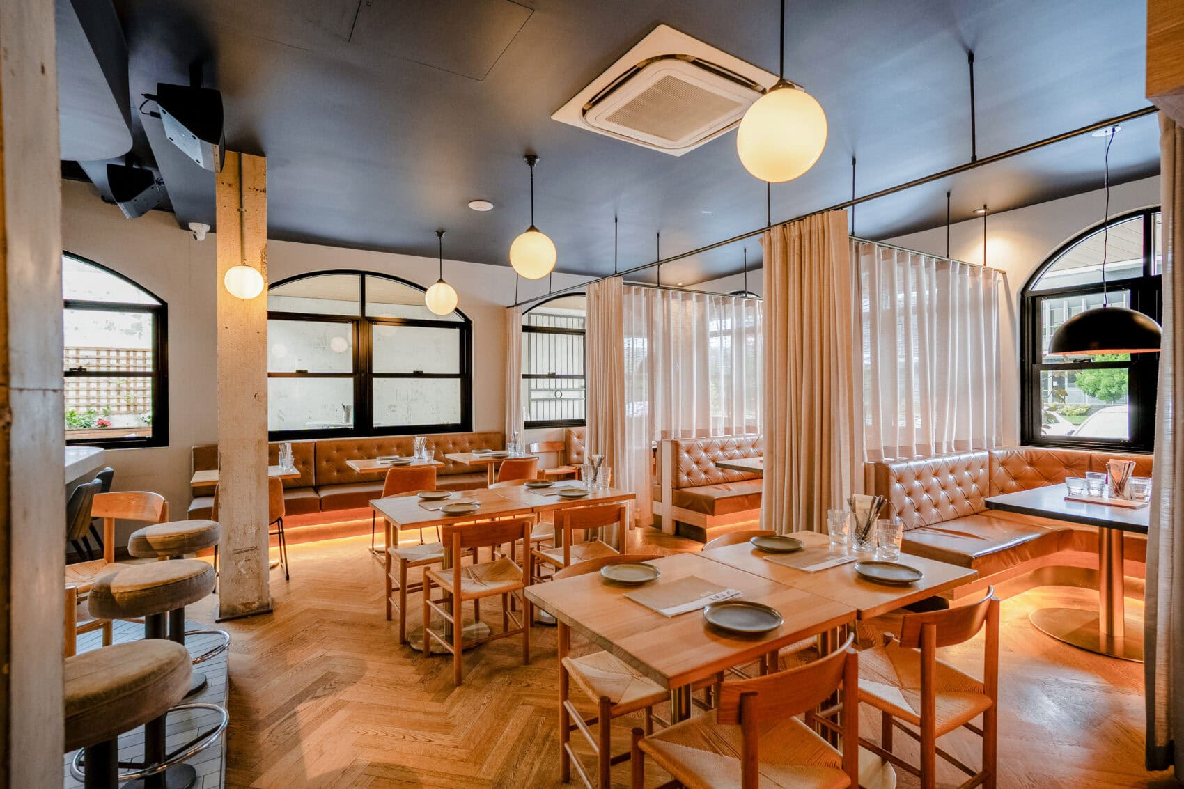 The interior view of Corbett & Claude Everton Park, with brown parquet style floor and brown tables, sectioned into booths by curtains.