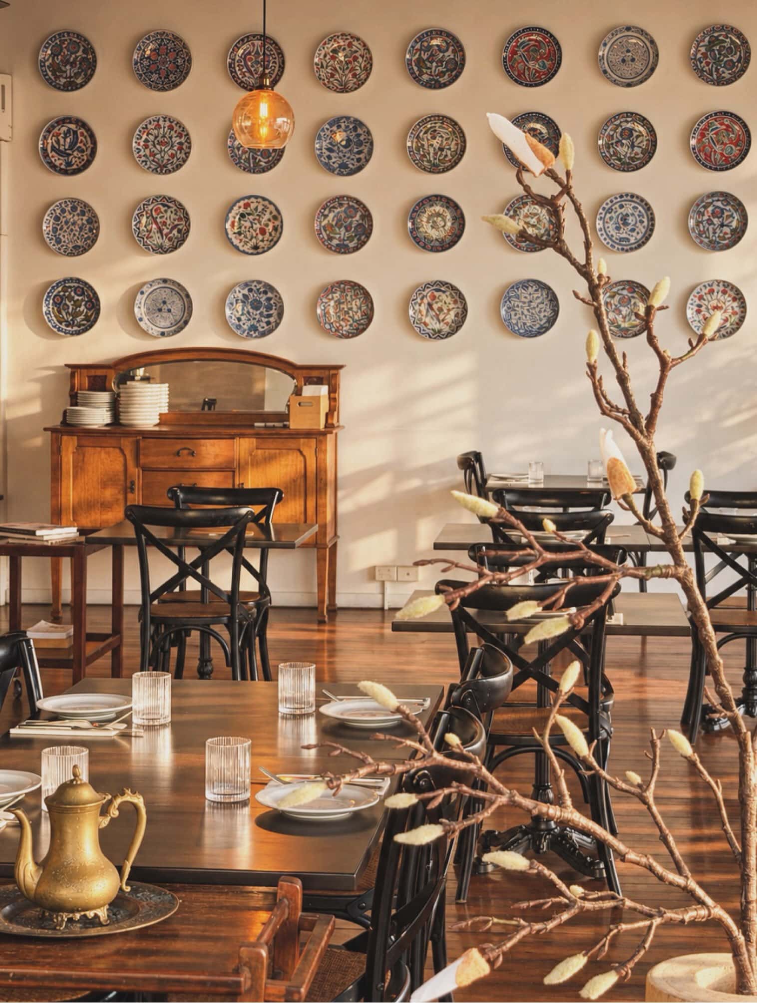 Warm brown tones inside of Olive Thyme restaurant in Brisbane, with brown tables, a bronze teapot and a dried plant.