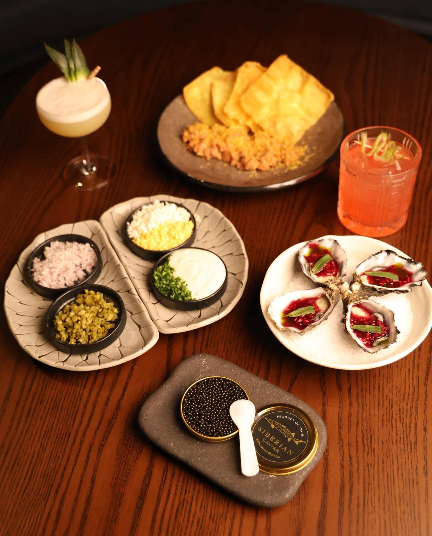Entree plates on a brown table of oysters, pita dips and caviar.