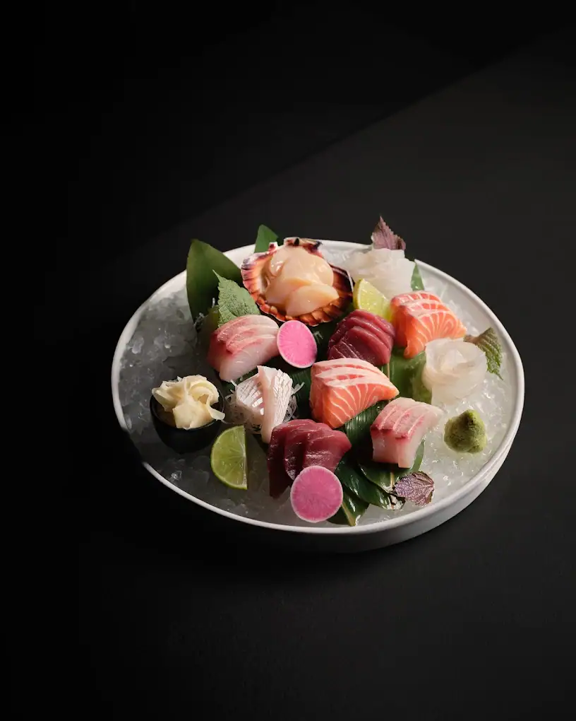 A colourful arrangement of sashimi, served on ice in a white bowl with a black background.