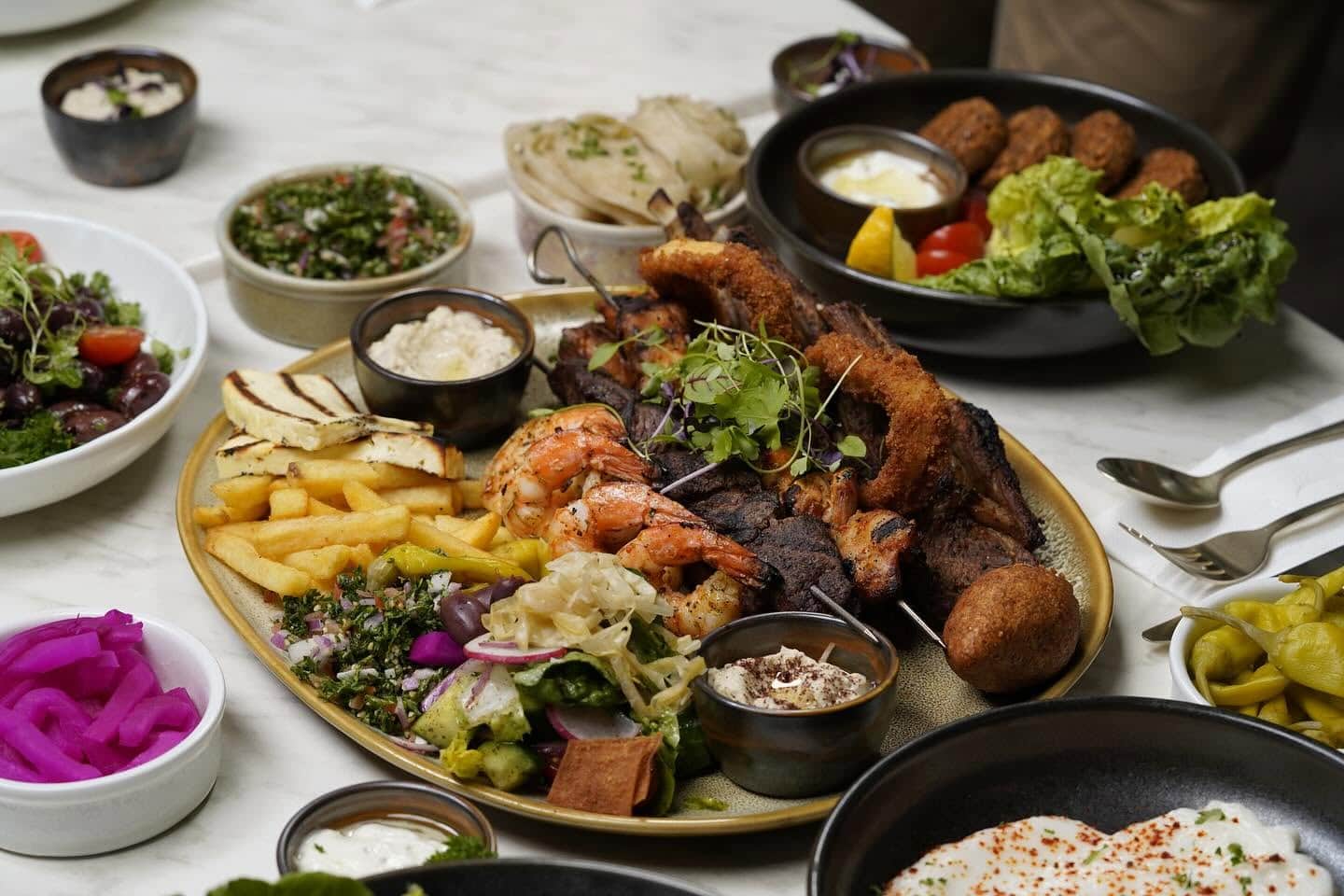 A Middle Eastern share platter of chips, pickled vegetables, skewered meats.