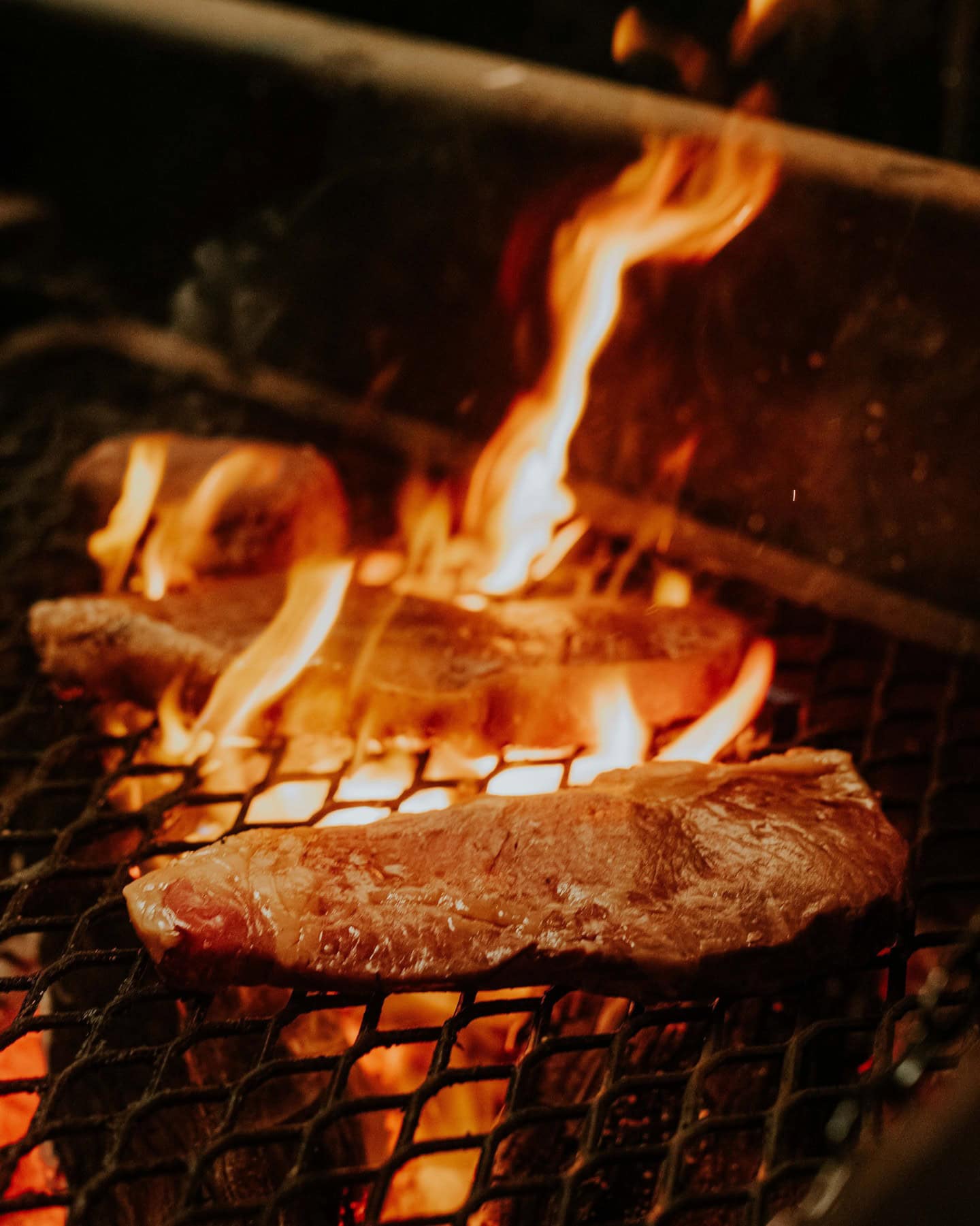 Two steaks being cooked over a flame, one is enveloped.