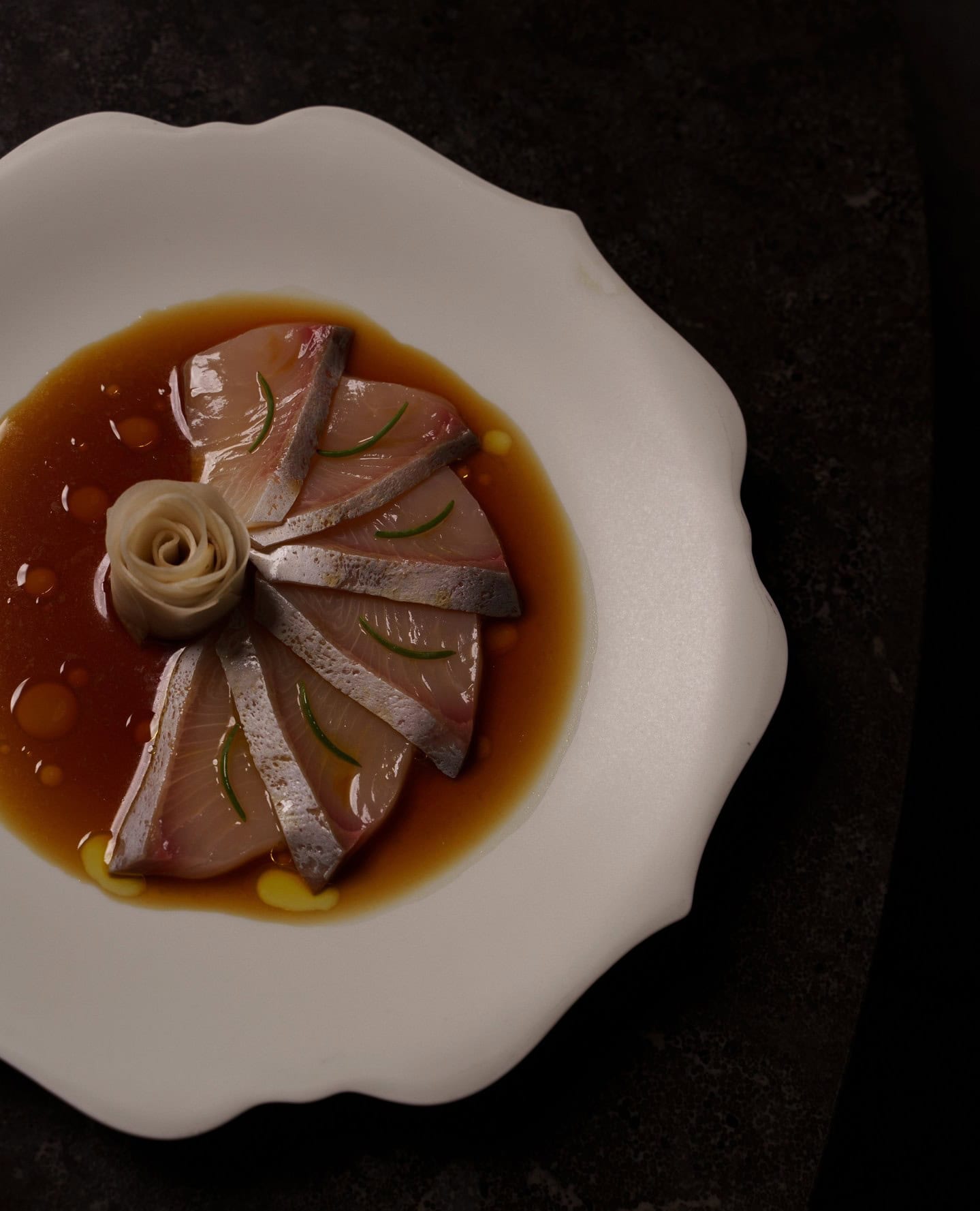 Kingfish ceviche artfully arranged on a curvy white place, with a light sauce dressing and a rosette of pickled ginger.