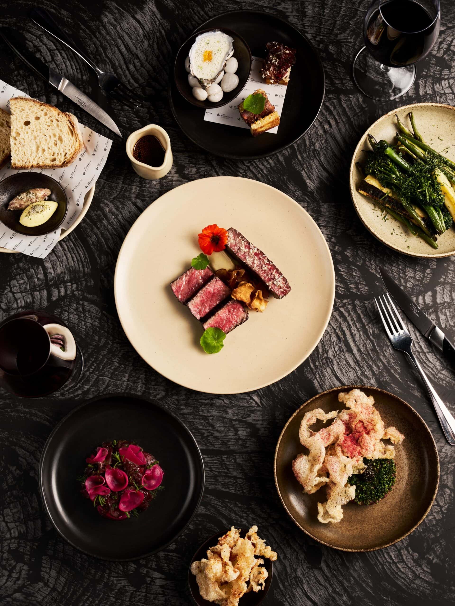 Fine dining spread at The Woodhouse in Bendigo, featuring steak, seasonal vegetables, oysters, bread and red wine.