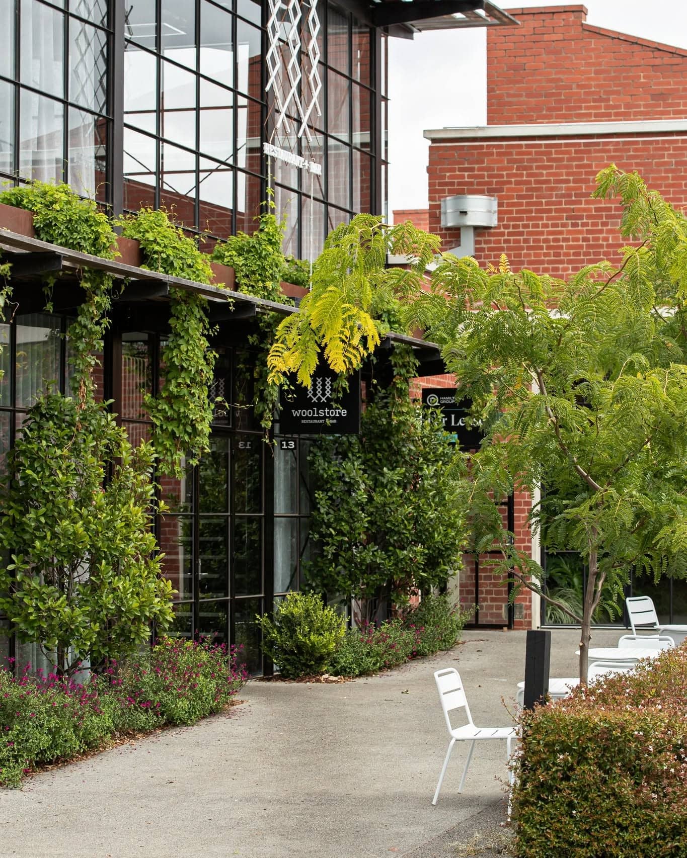 Exterior of Woolstore restaurant in Newtown, Geelong, set within a converted red-brick industrial building surrounded by greenery.