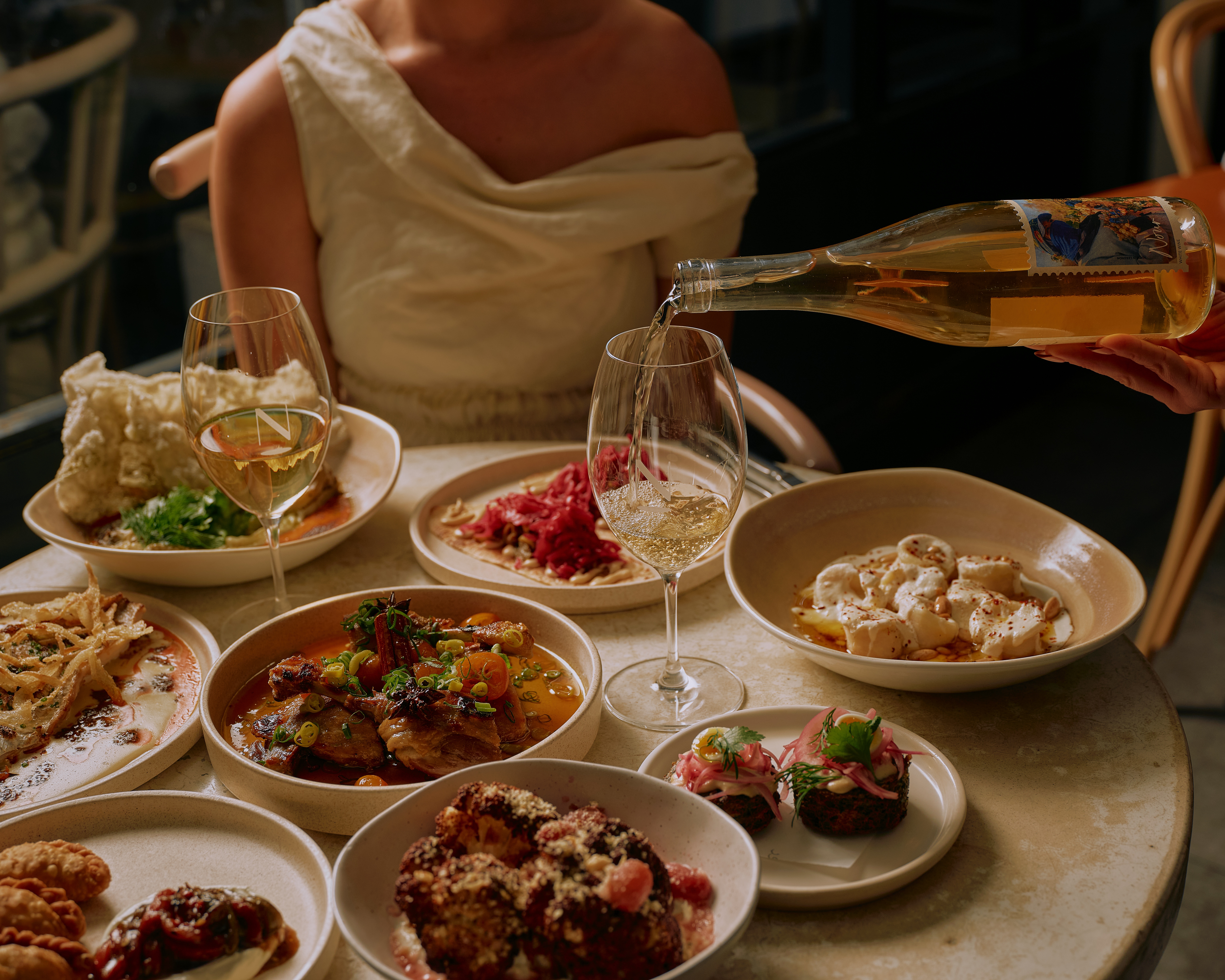Banquet spread of Middle Eastern dishes with wine being poured for Nour's 10th anniversary menu, Surry Hills, Sydney